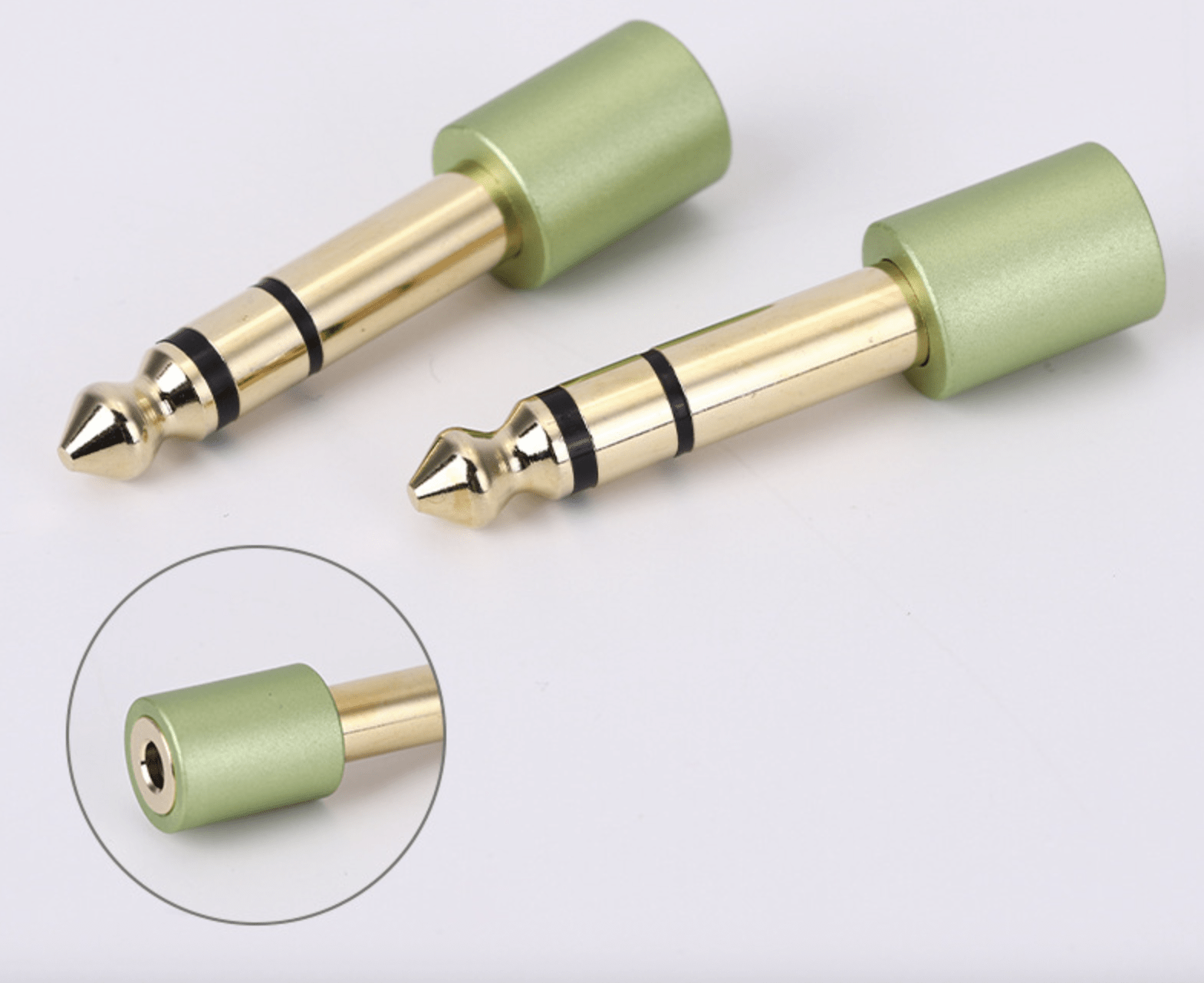 Two gold audio connectors with green sleeves on a white background