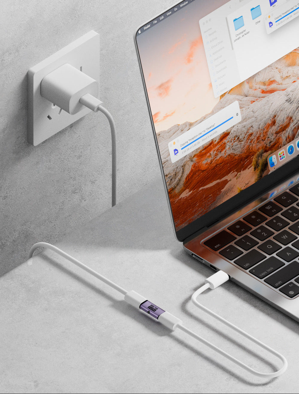 Laptop connected to a power outlet with a USB cable on a gray surface