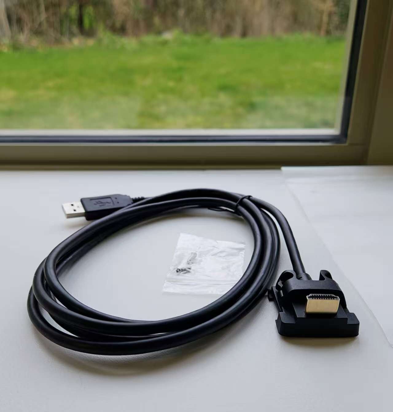 Black USB cable with connectors on a white surface near a window with greenery outside.