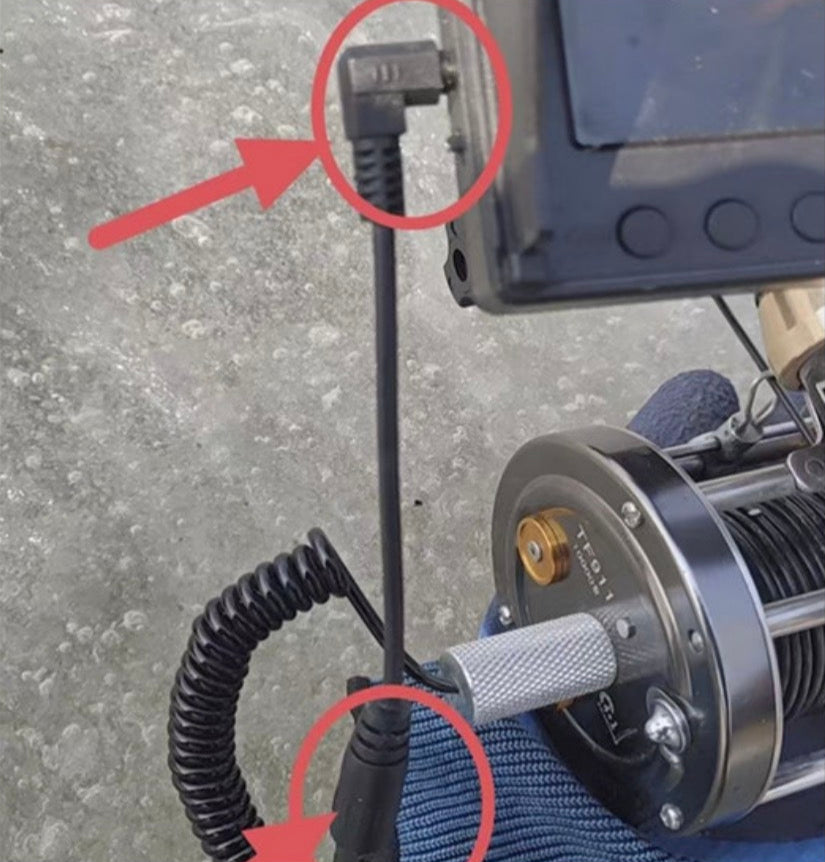Close-up of a winch with coiled cable and control box on a concrete surface.