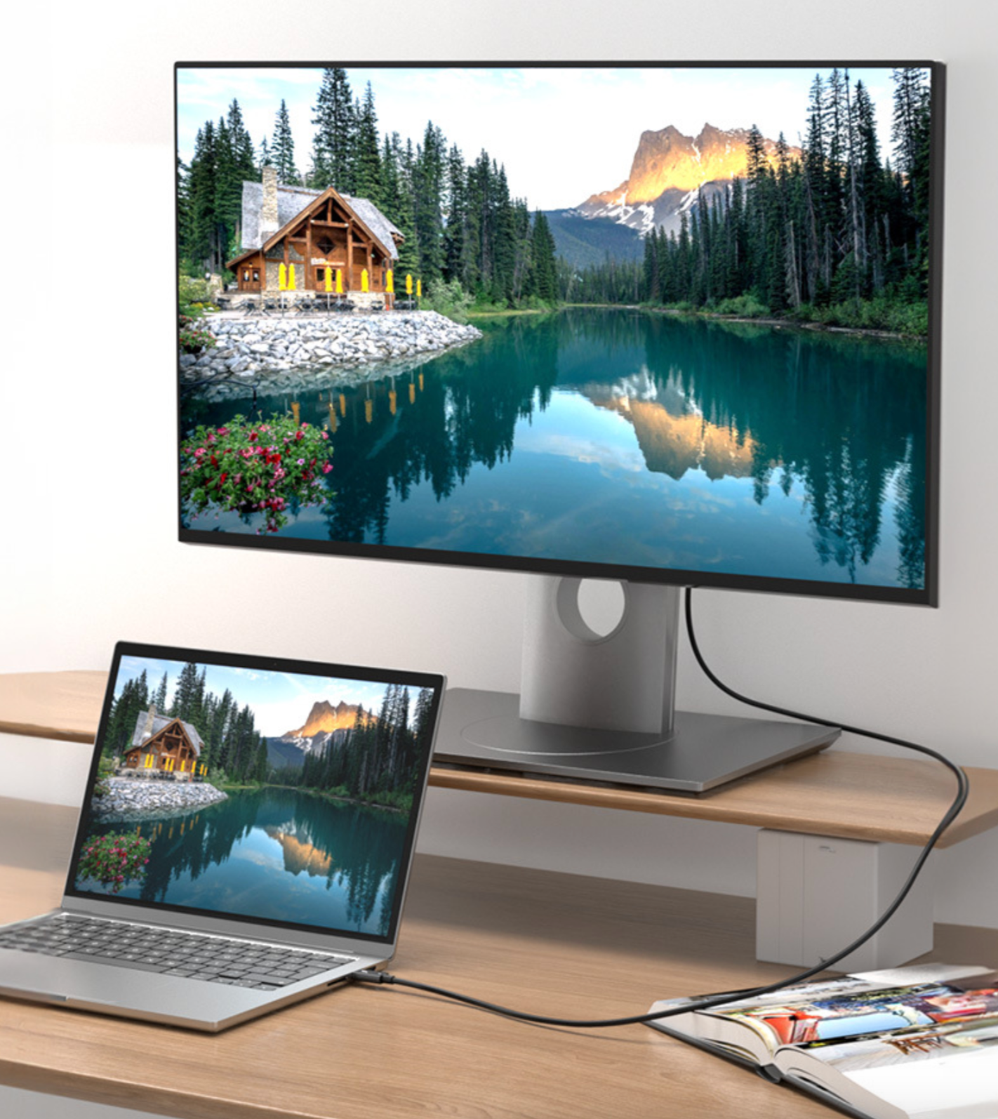 Monitor and laptop displaying a scenic view of a cabin by a lake.