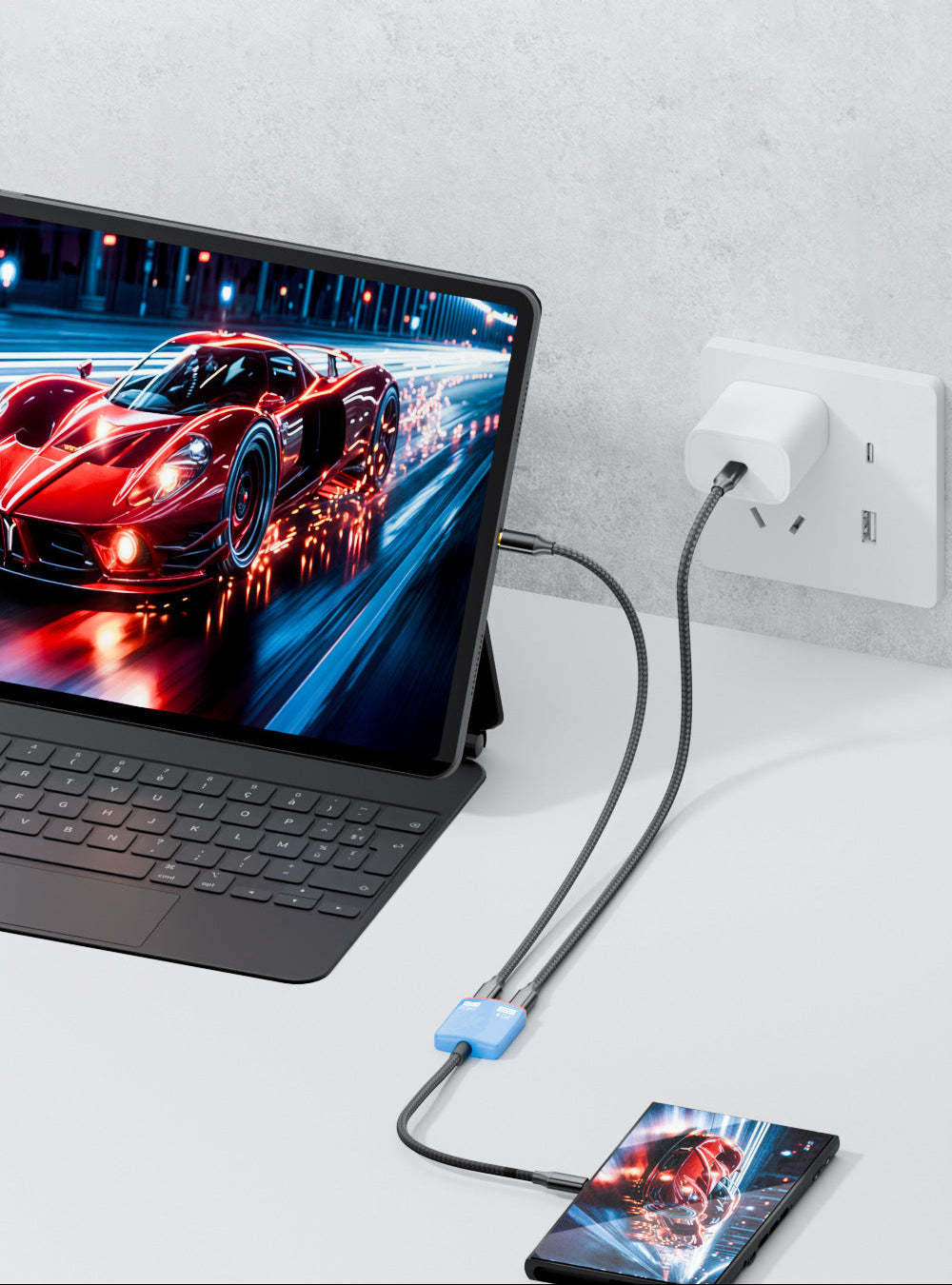 Laptop with a smartphone on a stand, connected to a power adapter, on a light gray surface.