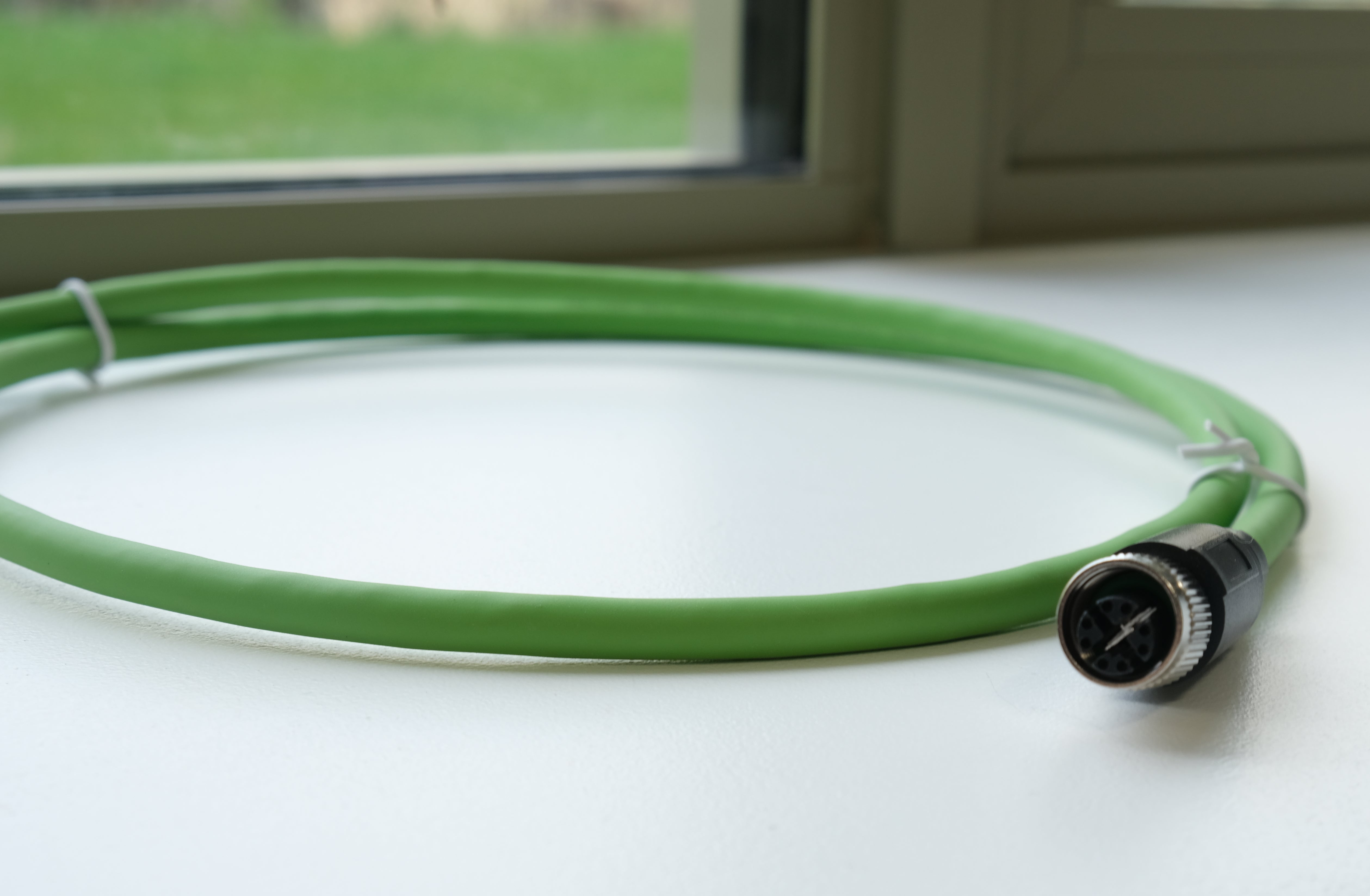 Green hose with a black fitting on a white surface near a window.