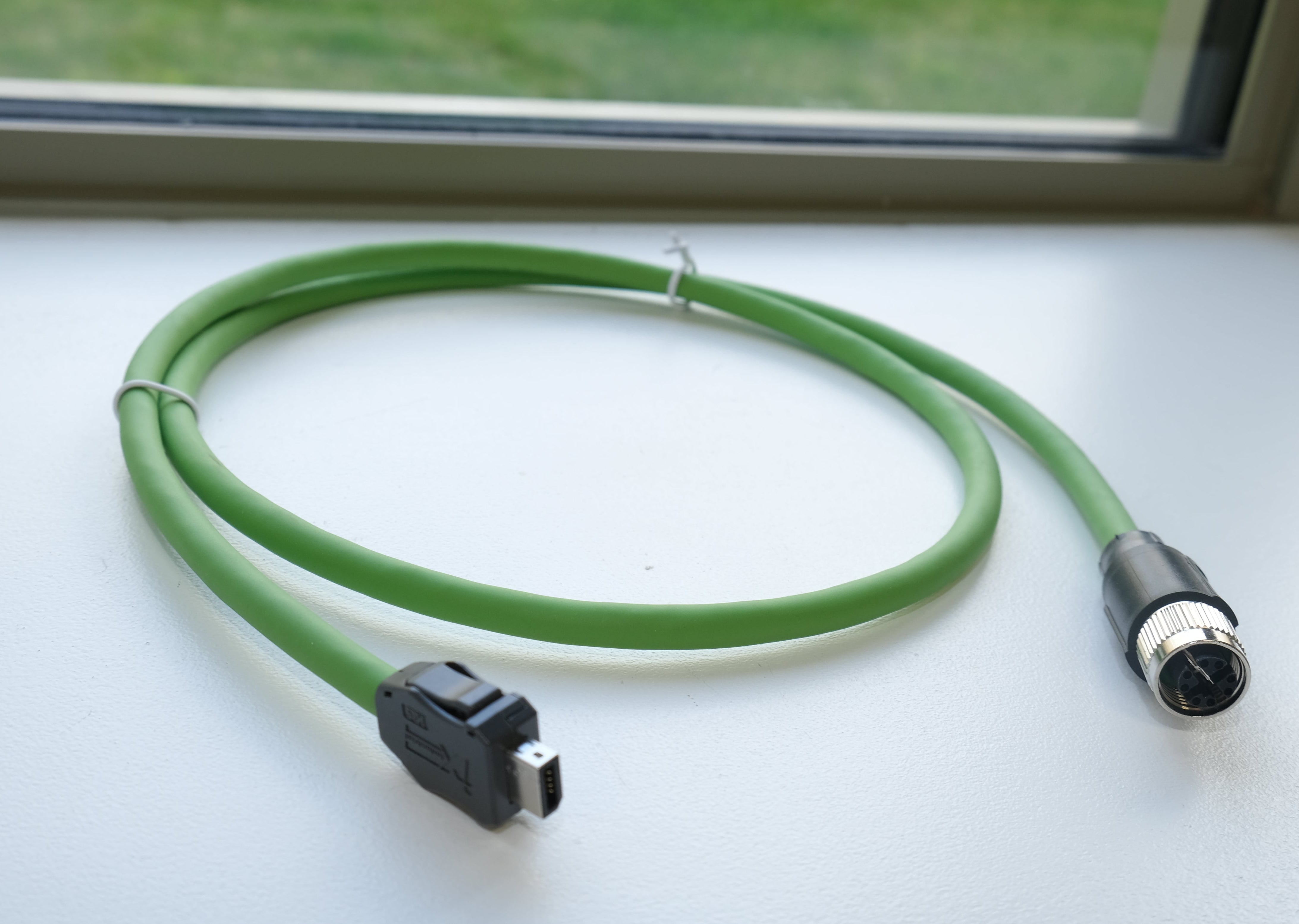 Green cable with connectors on a white surface near a window