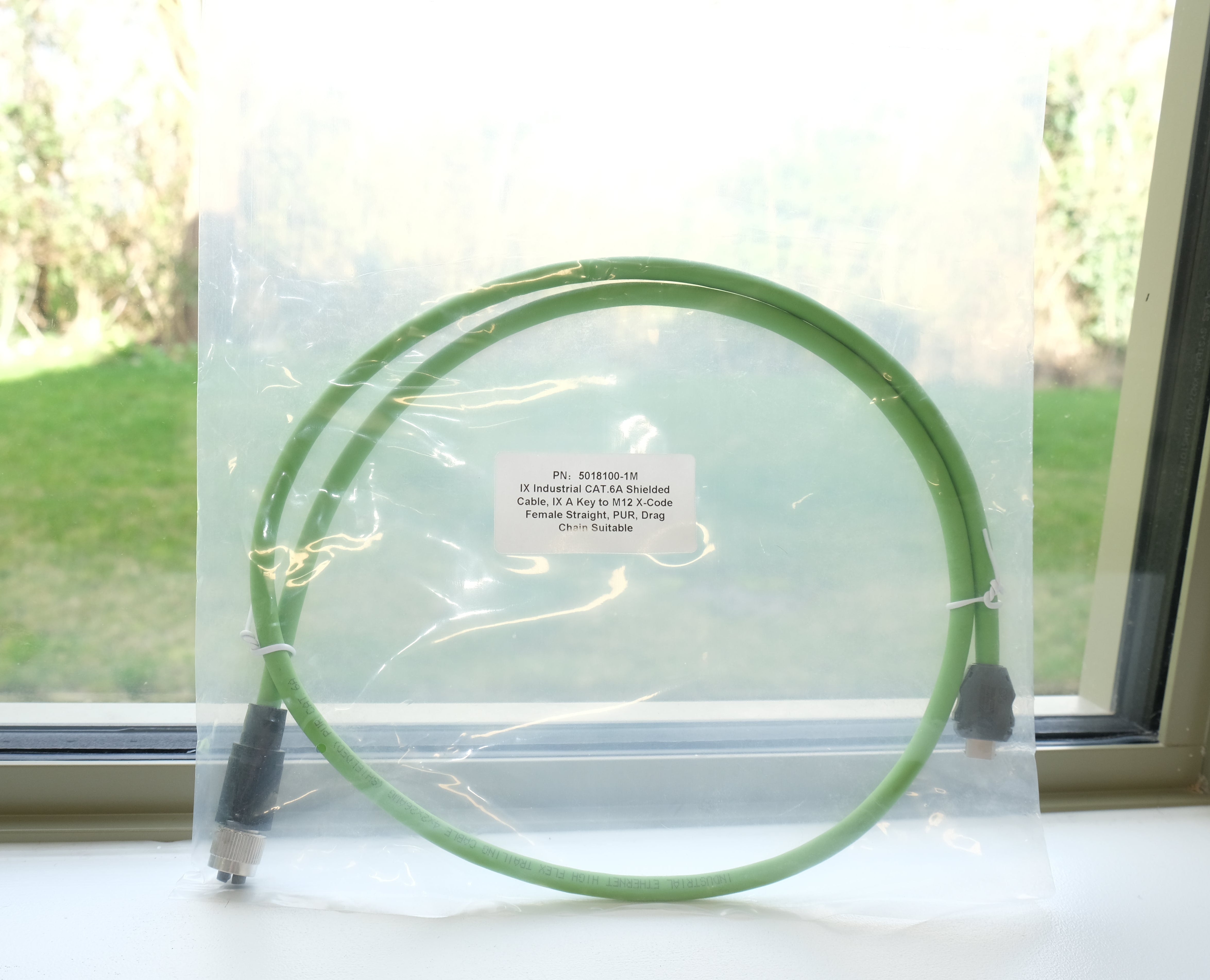 Green cable with a label on a white surface near a window with a view of grass.