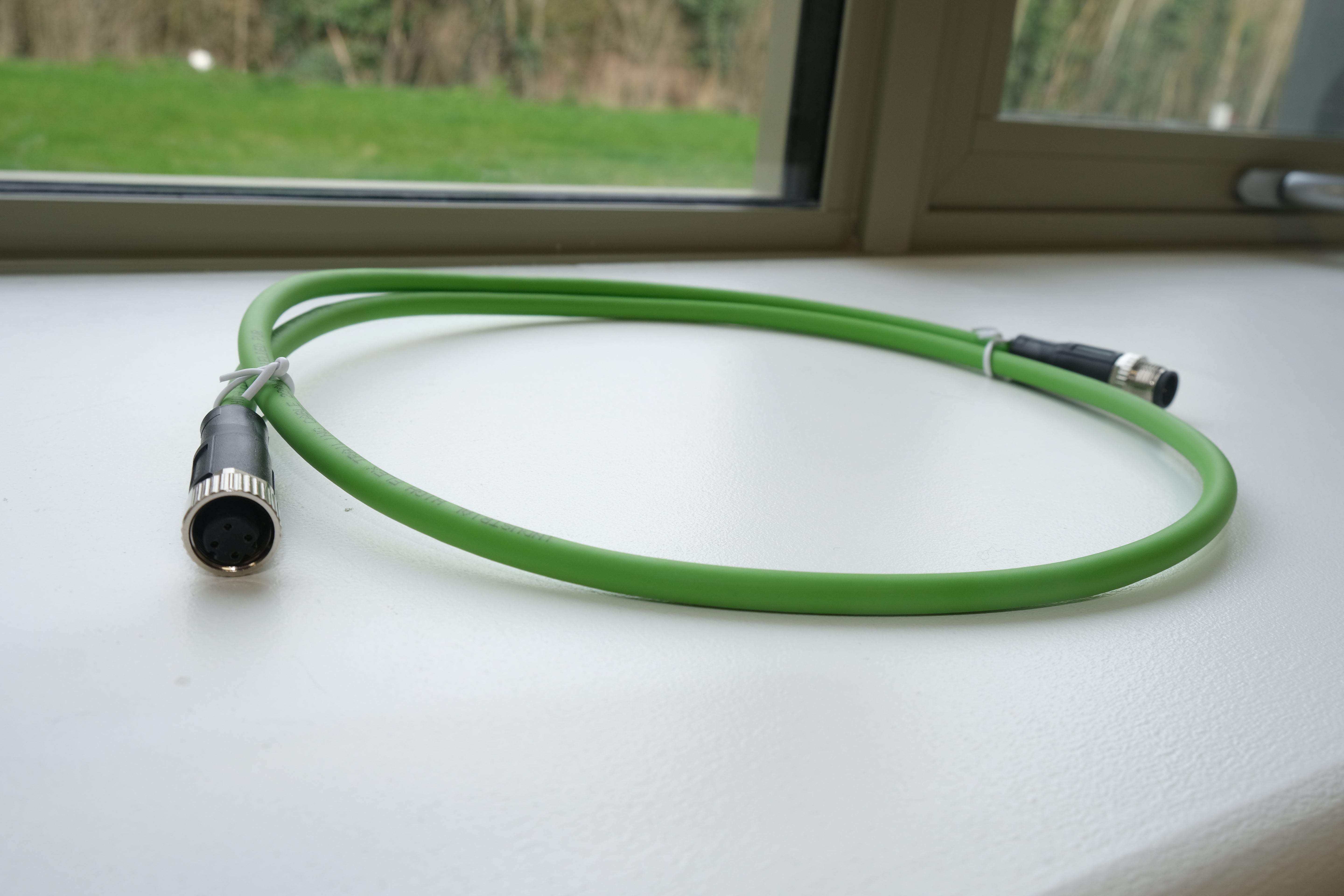 Green hose with connectors on a white surface, window in the background