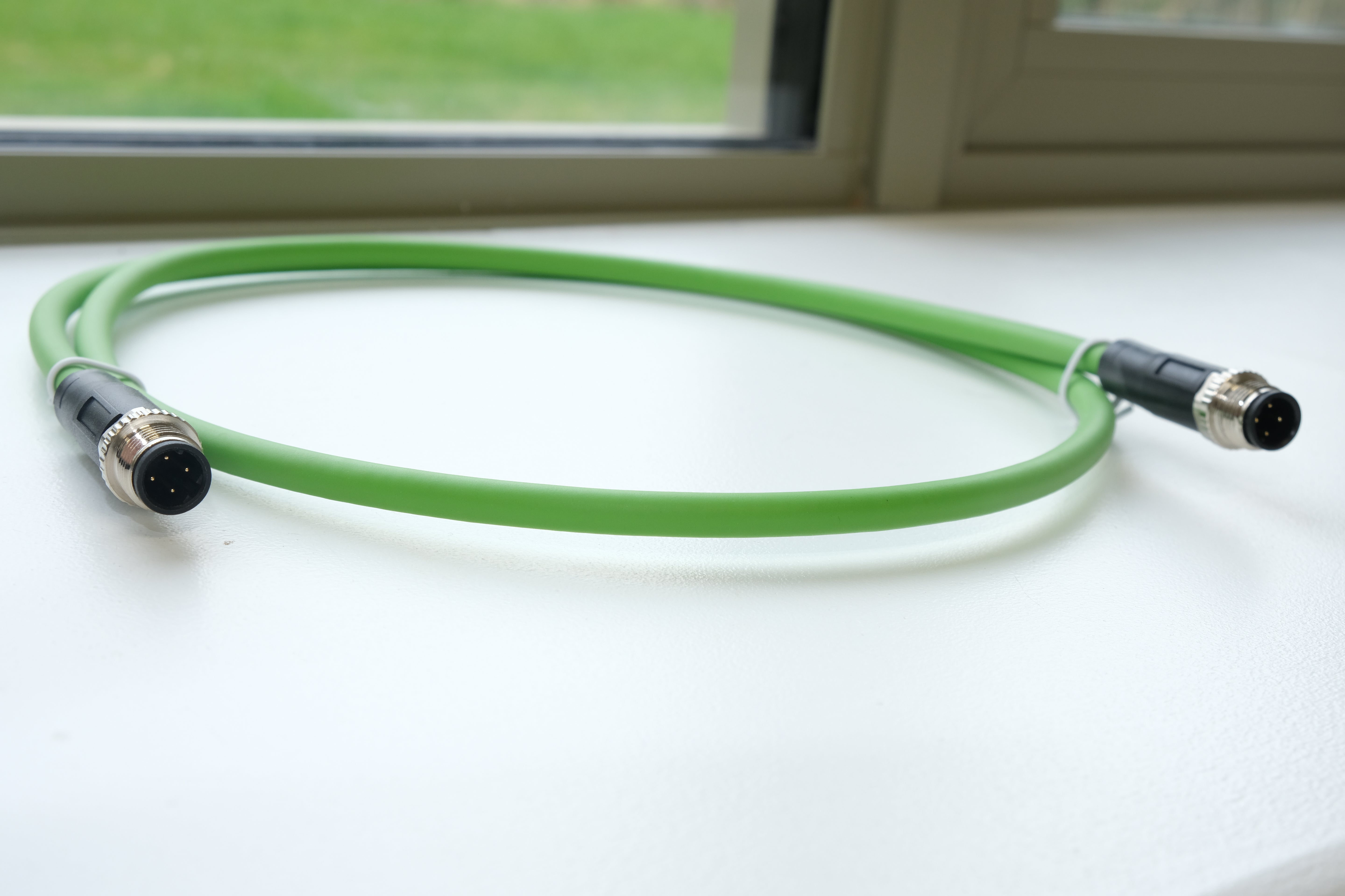 Green cable with connectors on a white surface near a window