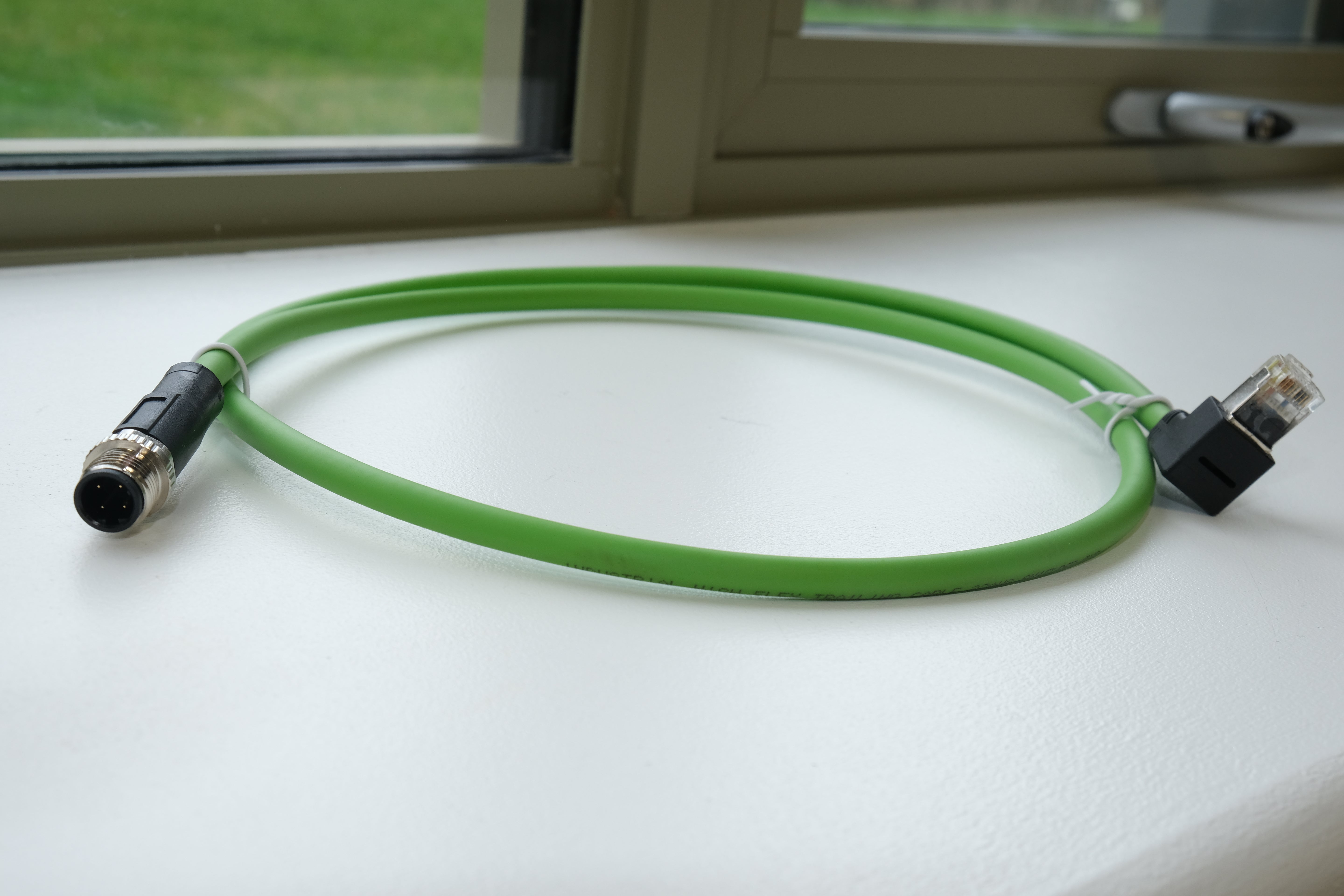 Green cable with connectors on a white surface near a window