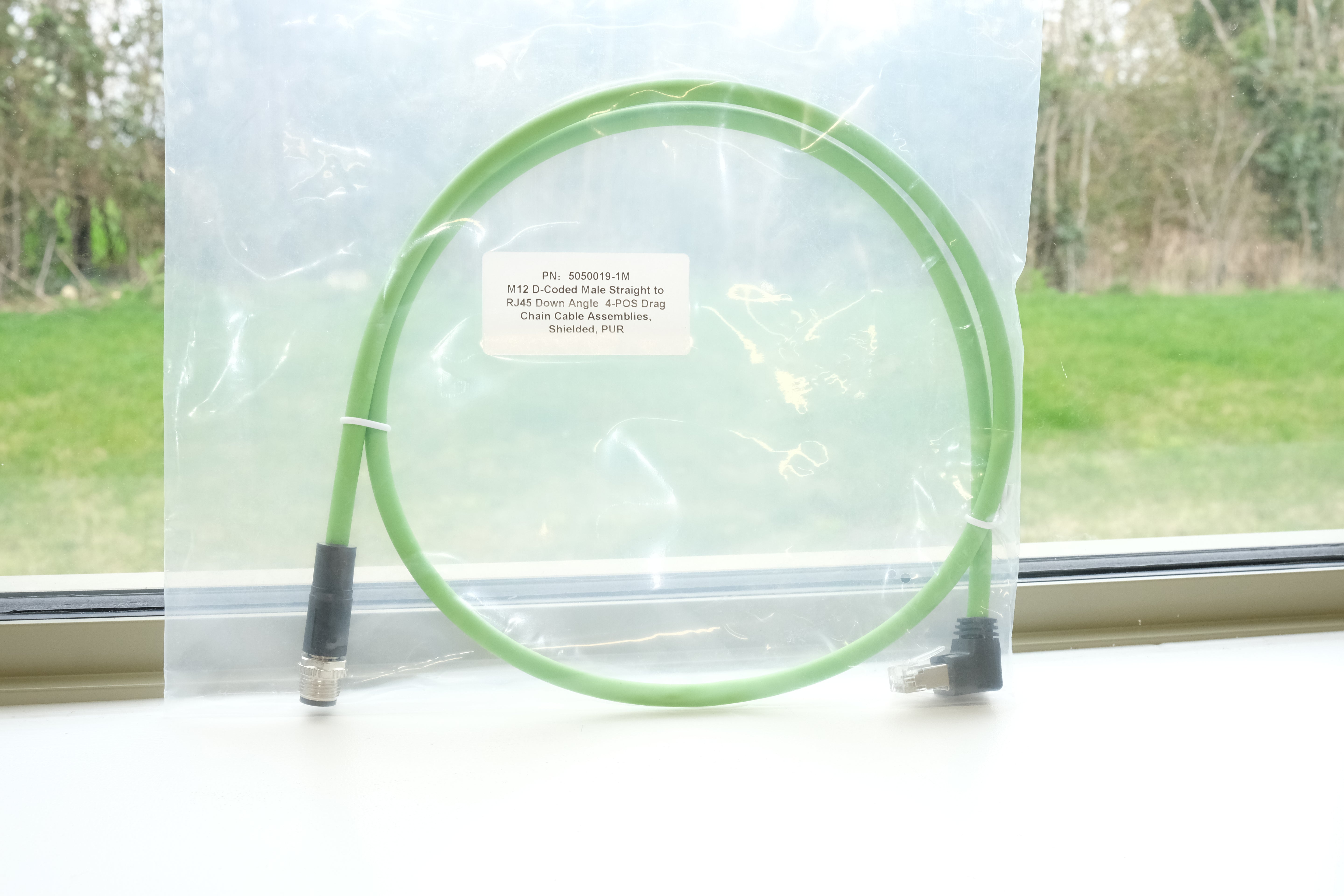 Green cable with a label on a white surface, with a window in the background showing greenery.