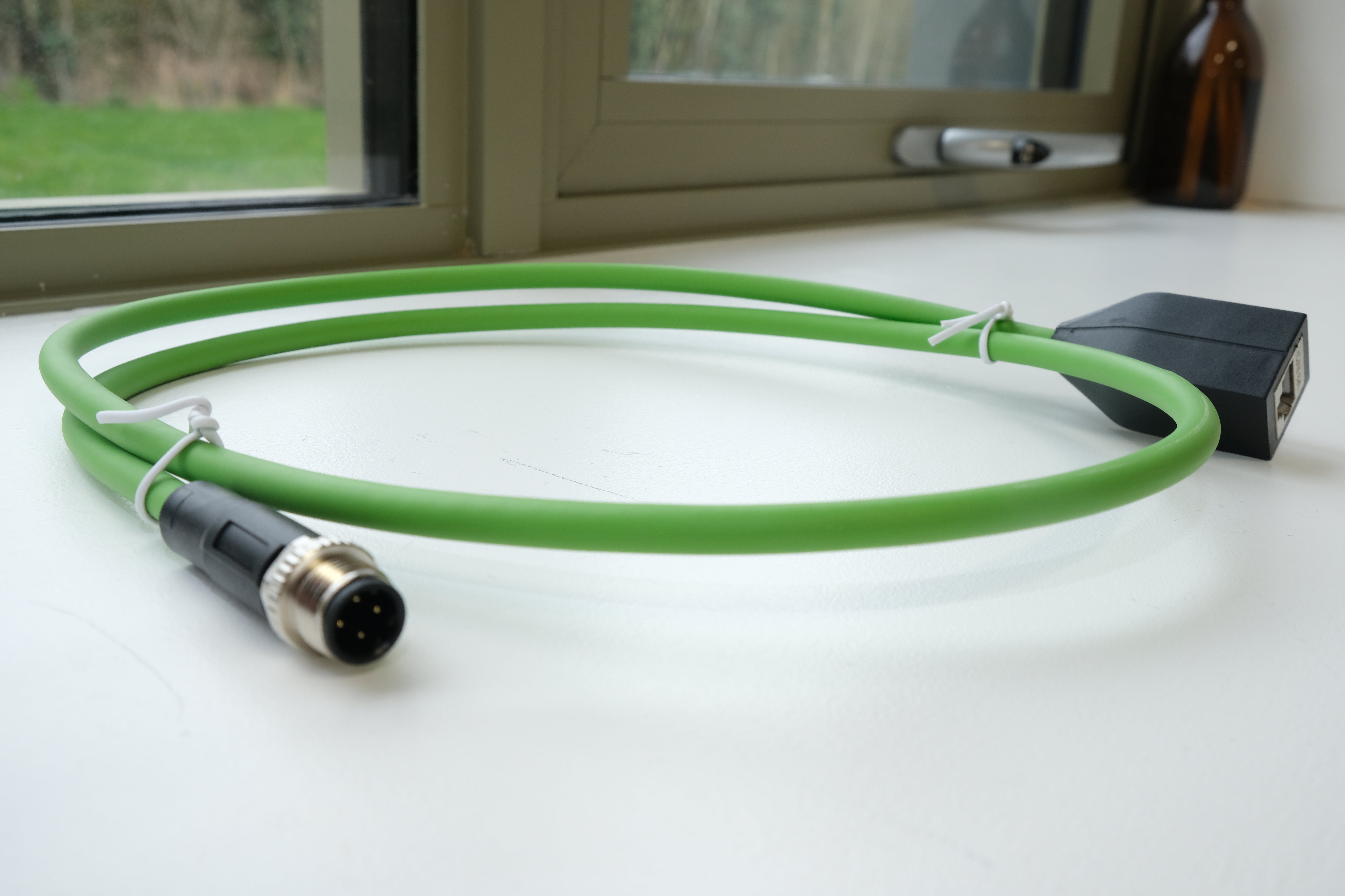 Green cable with connectors on a white surface near a window