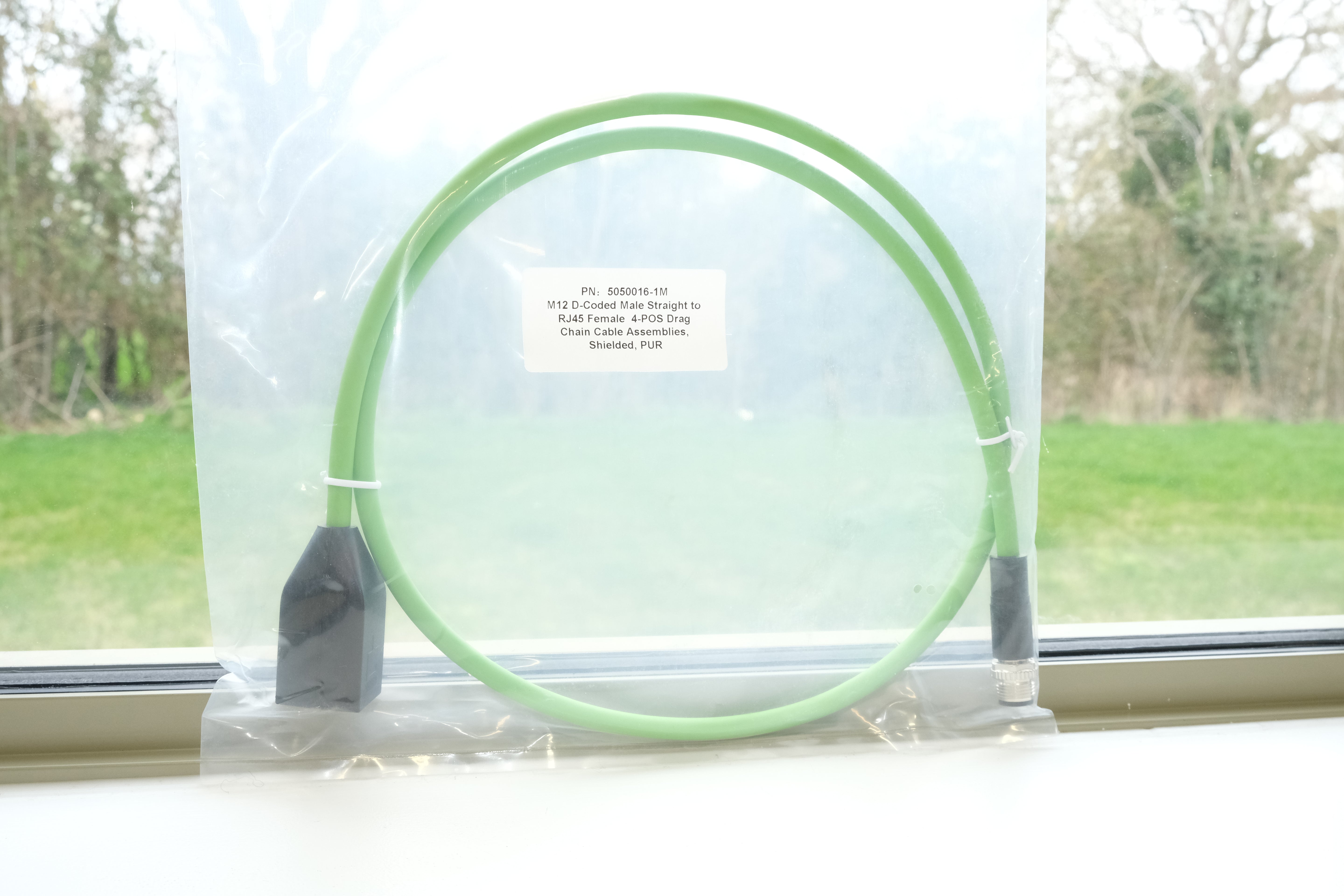 Green hoop with a label on a stand in front of a window with a view of trees and grass.