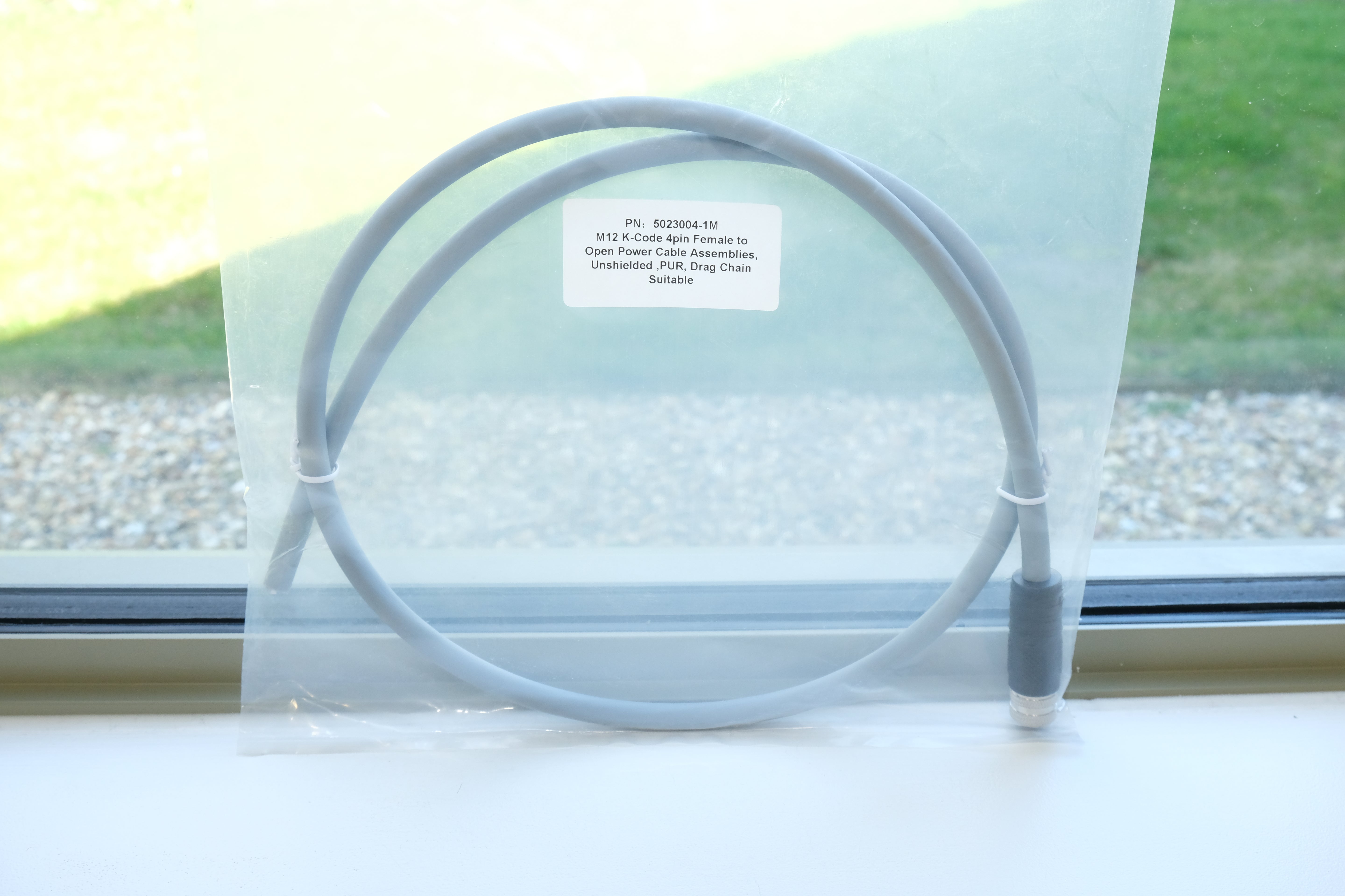 Clear plastic bag with a gray cable inside, on a windowsill with grass outside.