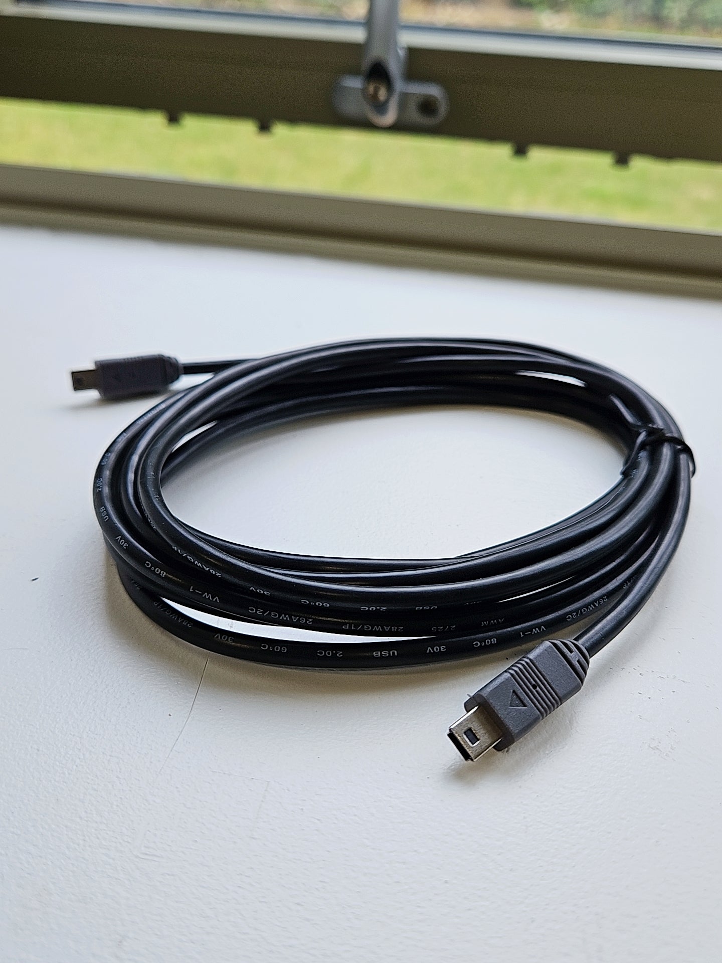Coiled black USB cable on a white surface with a window in the background