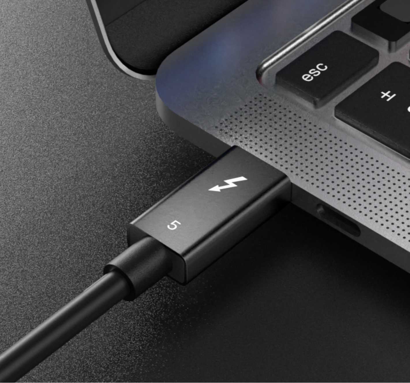 Black USB-C cable connected to a laptop on a dark surface