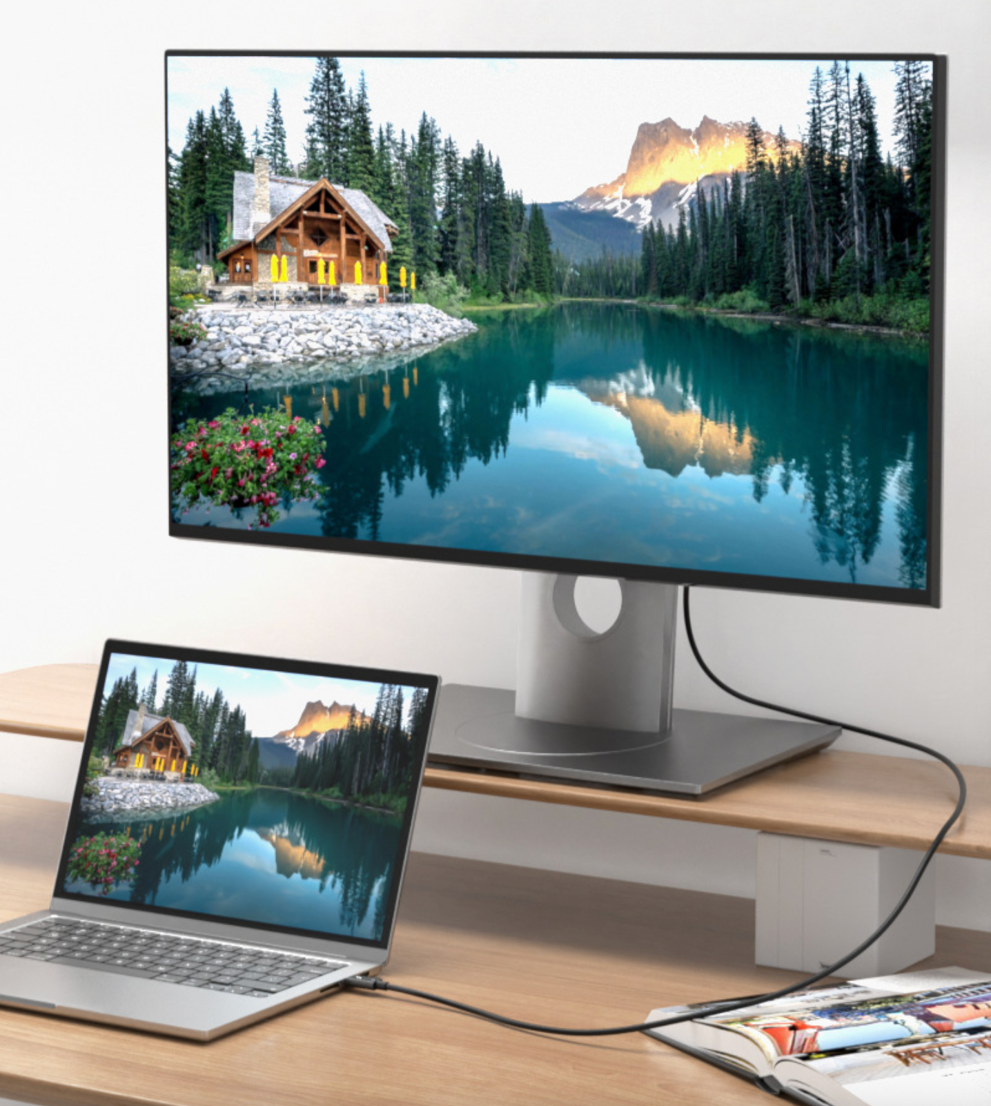 Monitor and laptop displaying a scenic view of a lake and cabin on a wooden desk.