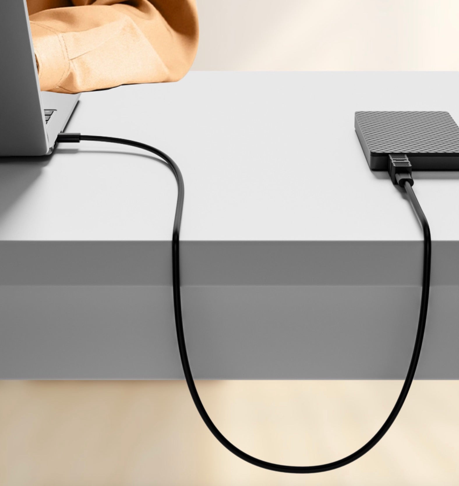 Laptop connected to an external hard drive via a cable on a desk.