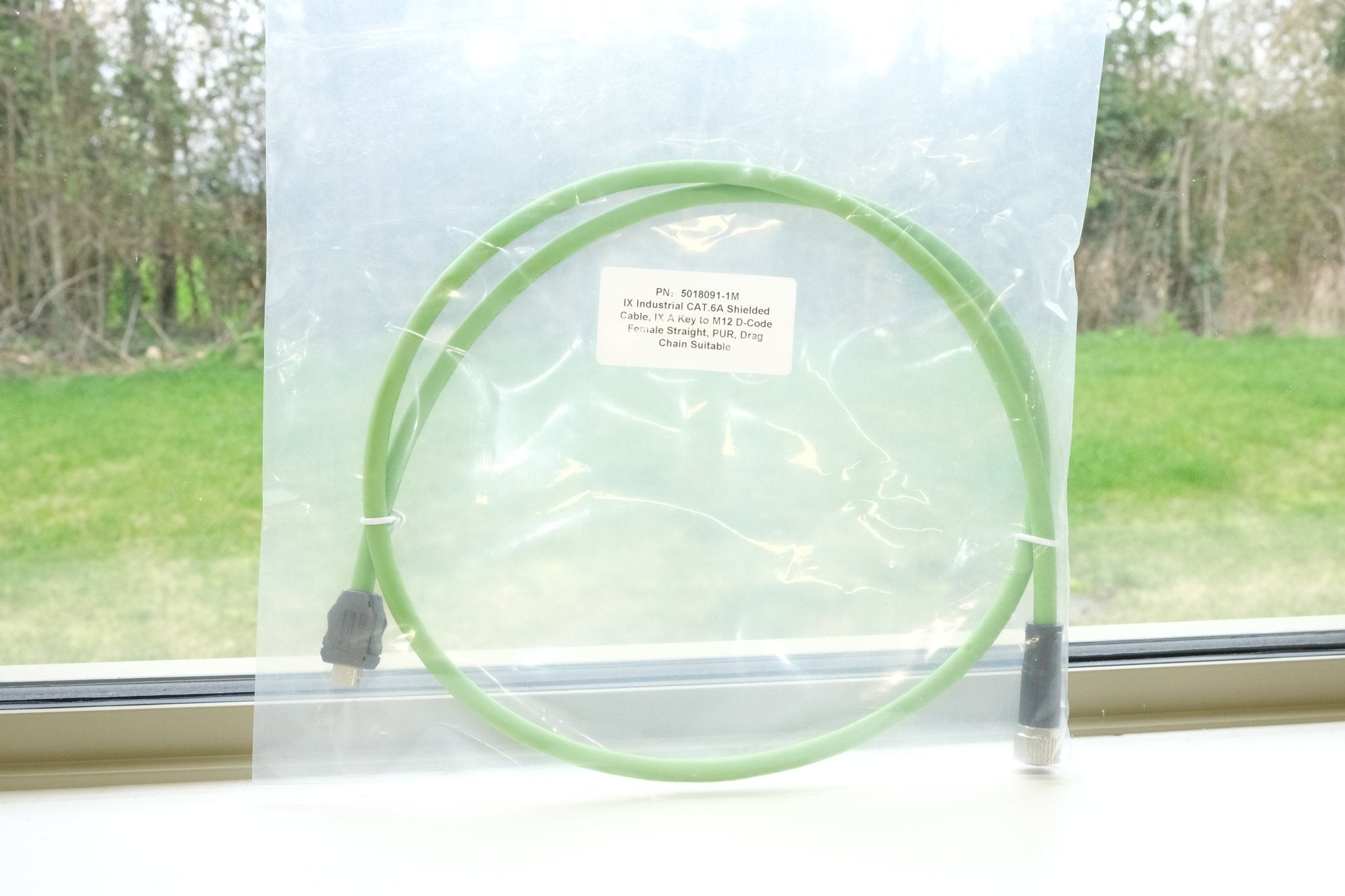Green cable in a clear plastic bag on a windowsill with a view of trees outside.
