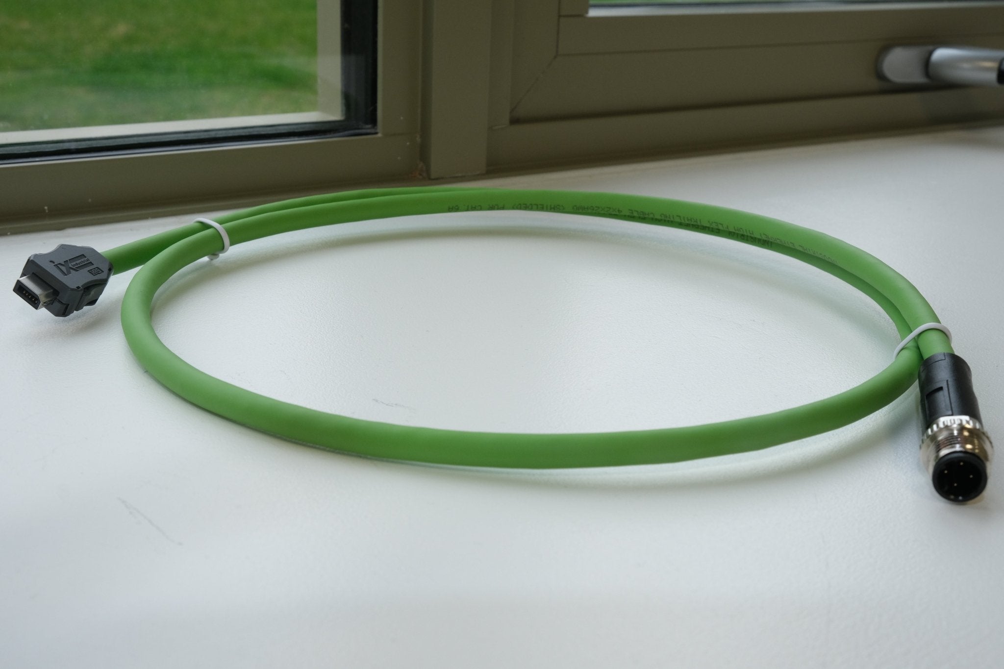 Green cable with connectors on a white surface near a window