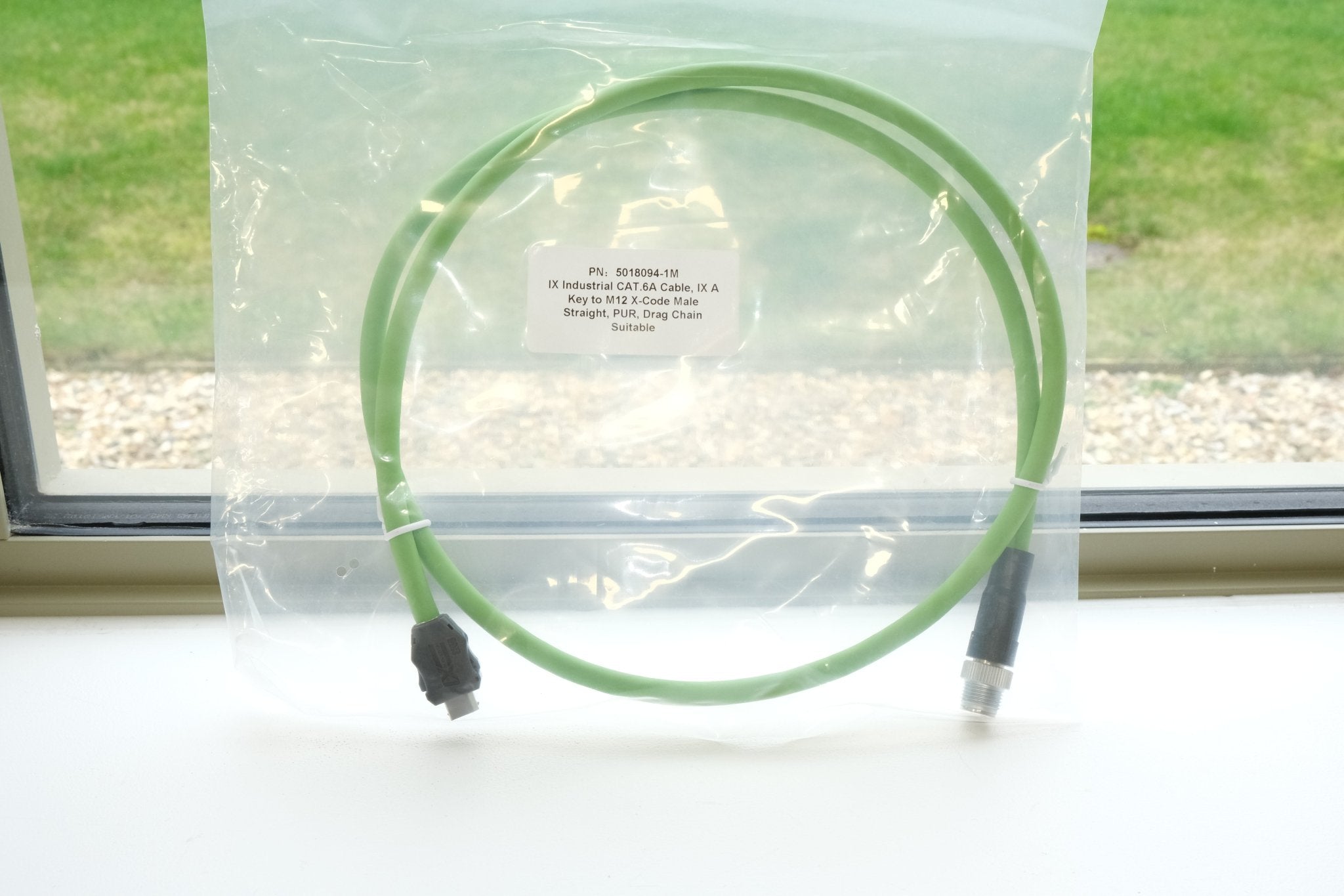 Green cable coiled on a white surface with a window in the background