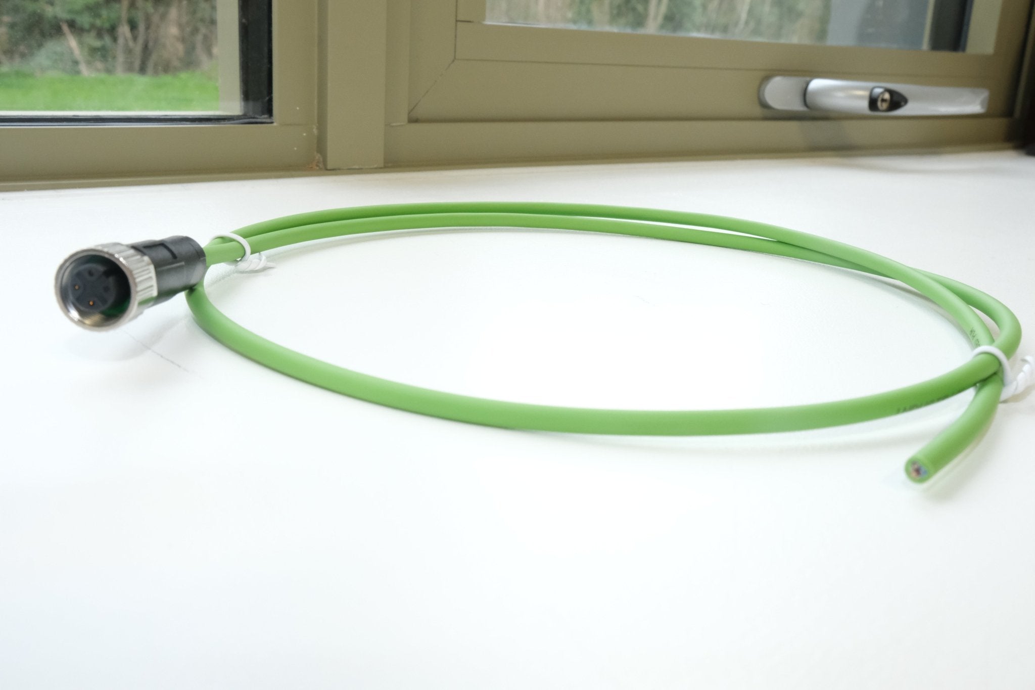 Green cable with a metallic connector on a white surface, with a window and door in the background.
