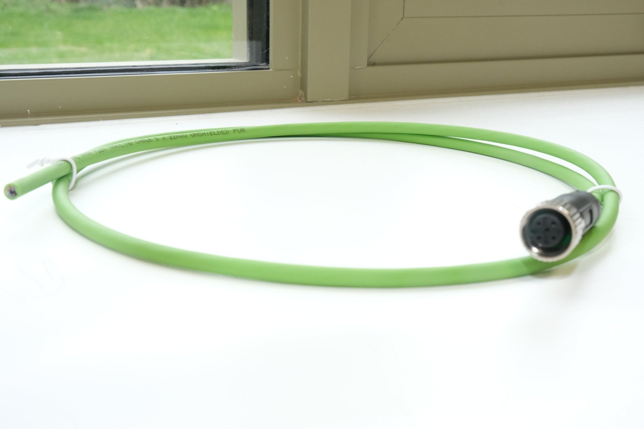 Green cable with a connector on a white surface near a window.