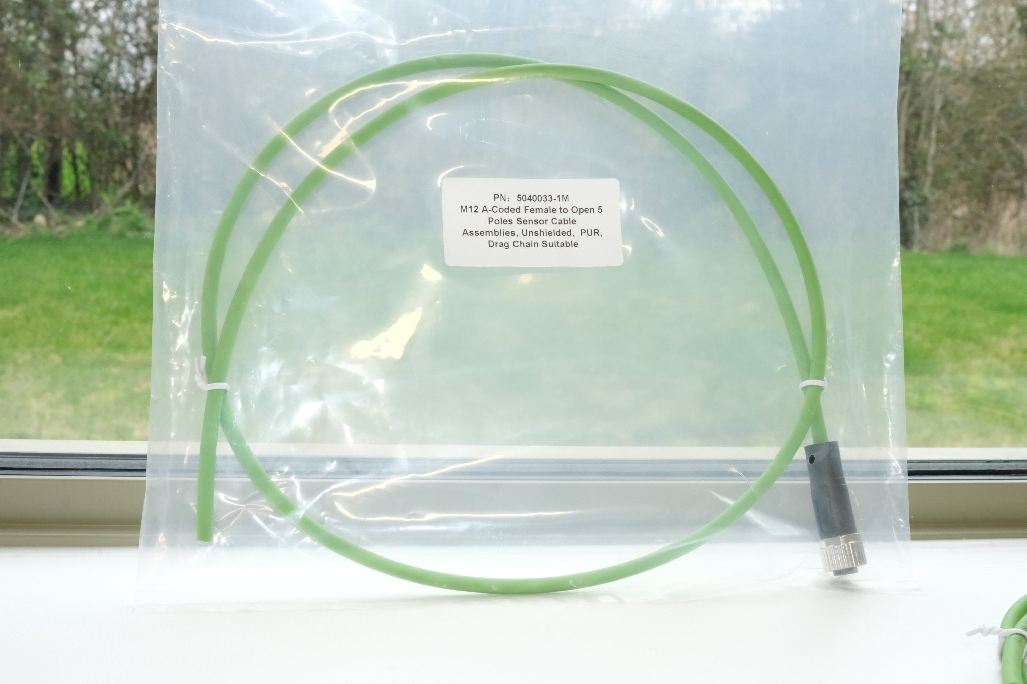 Green cable in a clear plastic bag with a label on a windowsill.