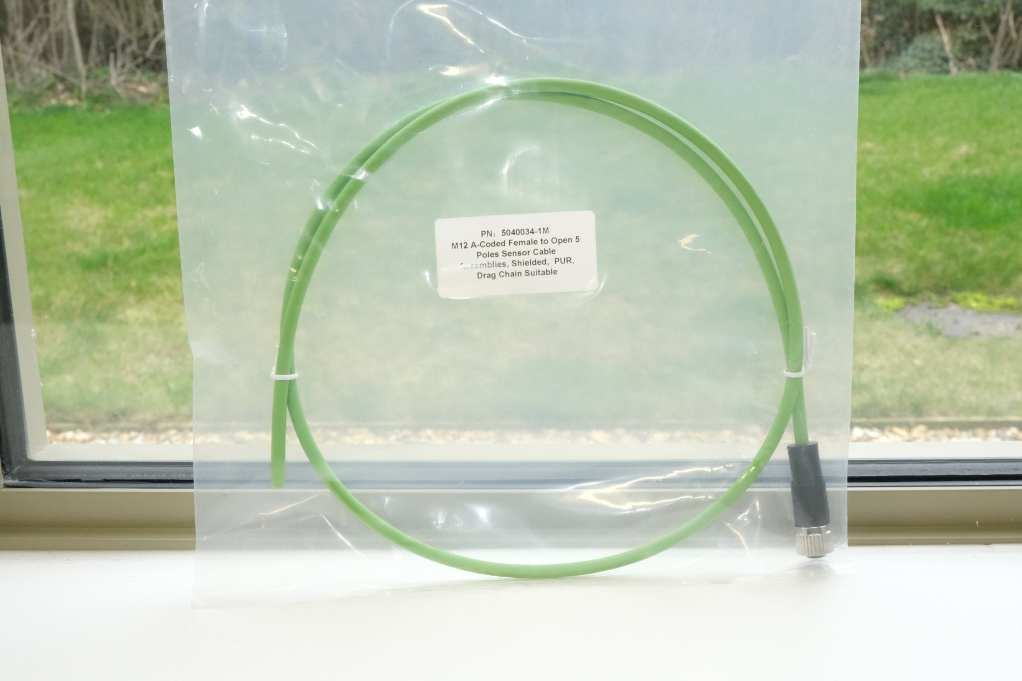 Green cable coiled on a clear plastic stand with a label, against a window background.