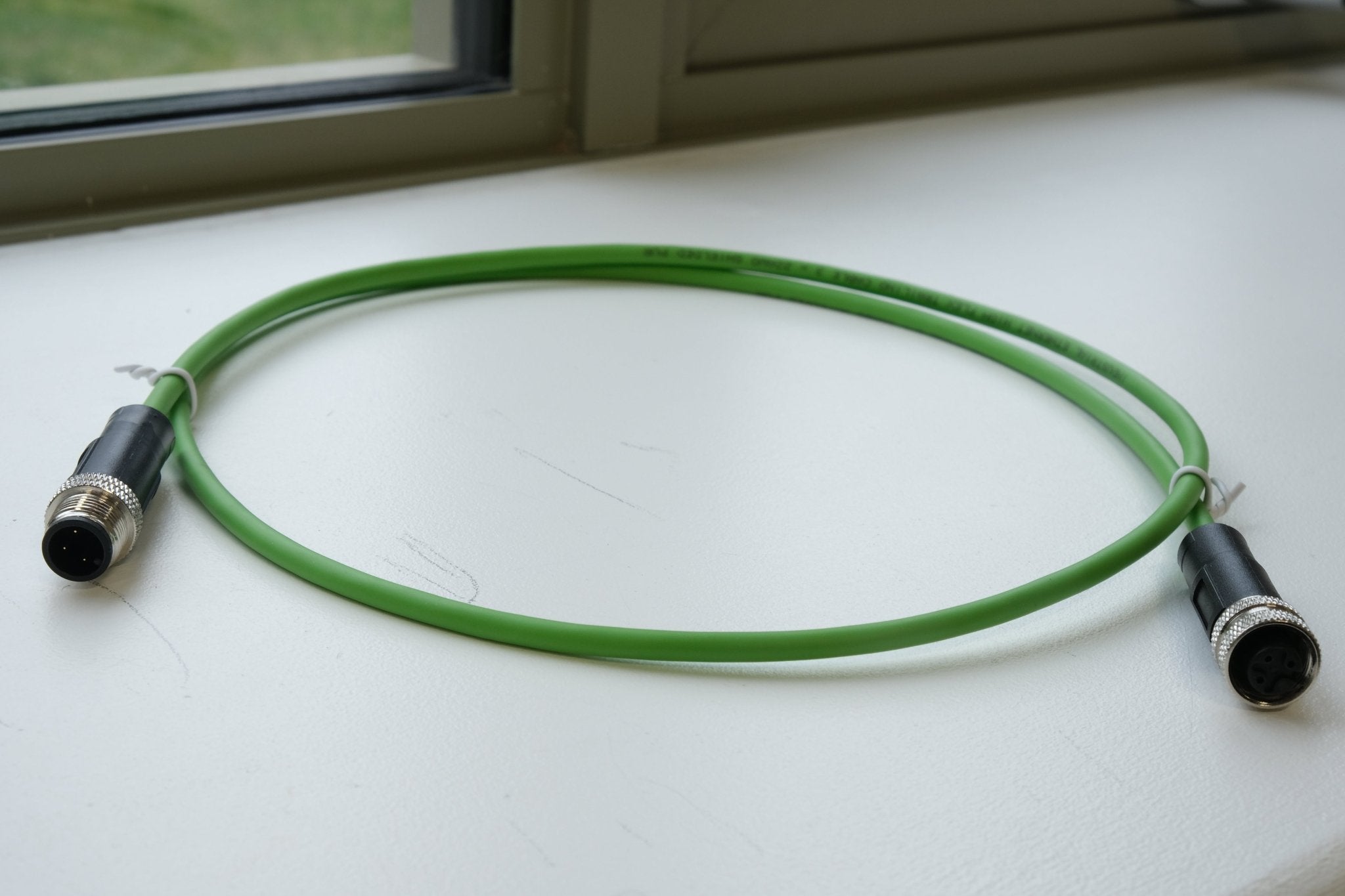 Green cable with connectors on a white surface near a window