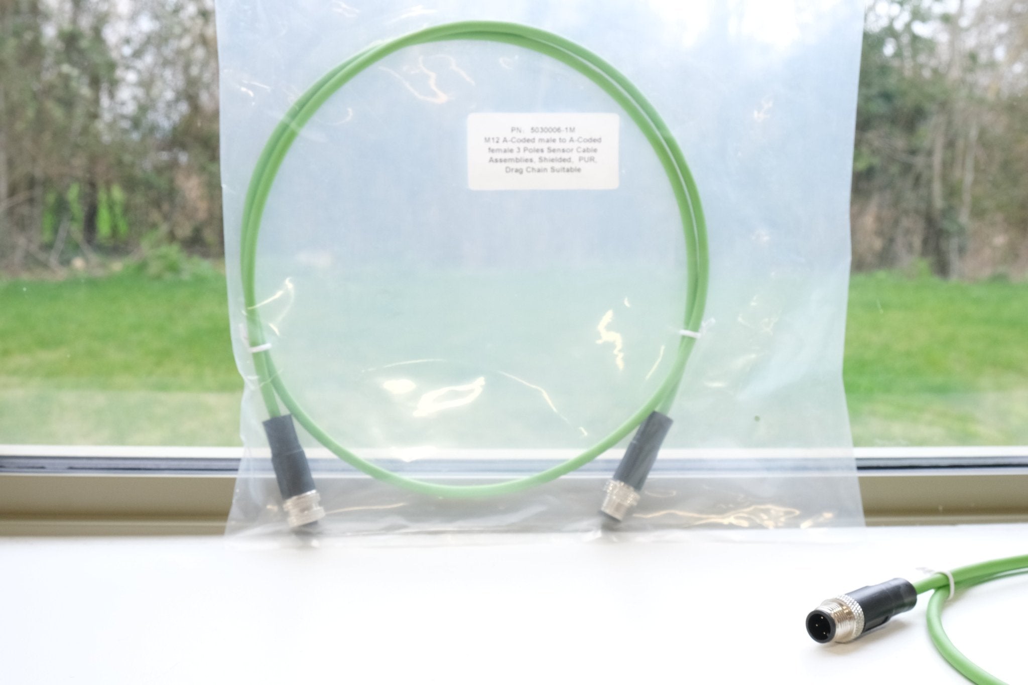 Green cable with connectors on a white surface, with a window in the background showing a grassy area.