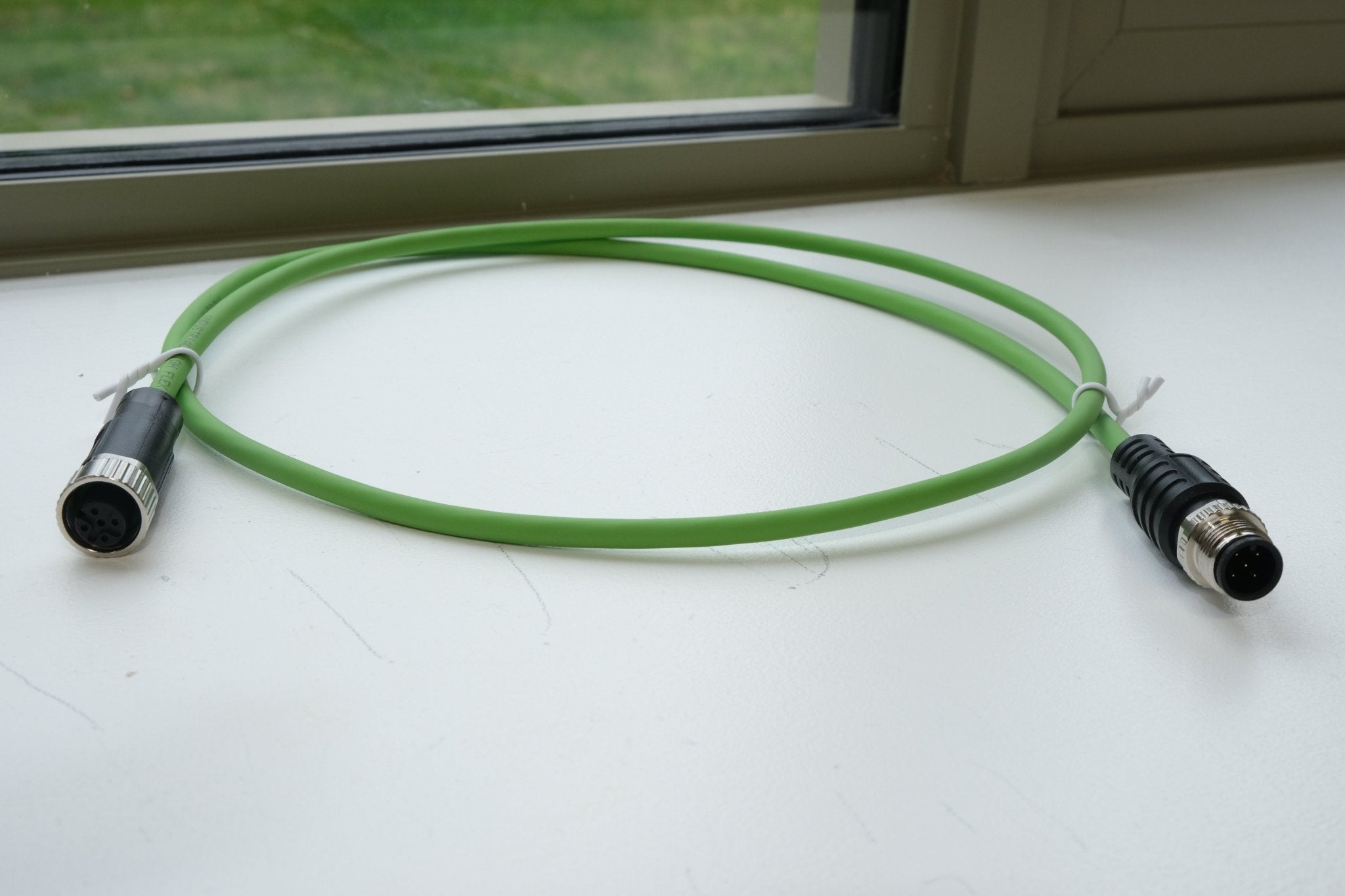 Green cable with connectors on a white surface near a window