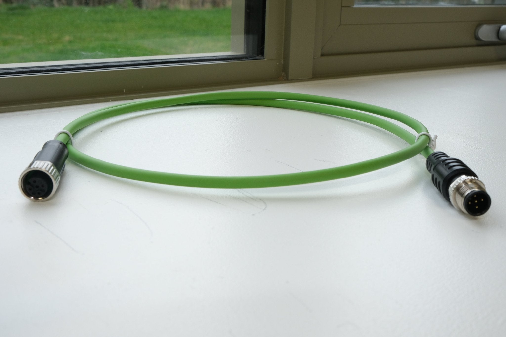 Green cable with connectors on a white surface near a window