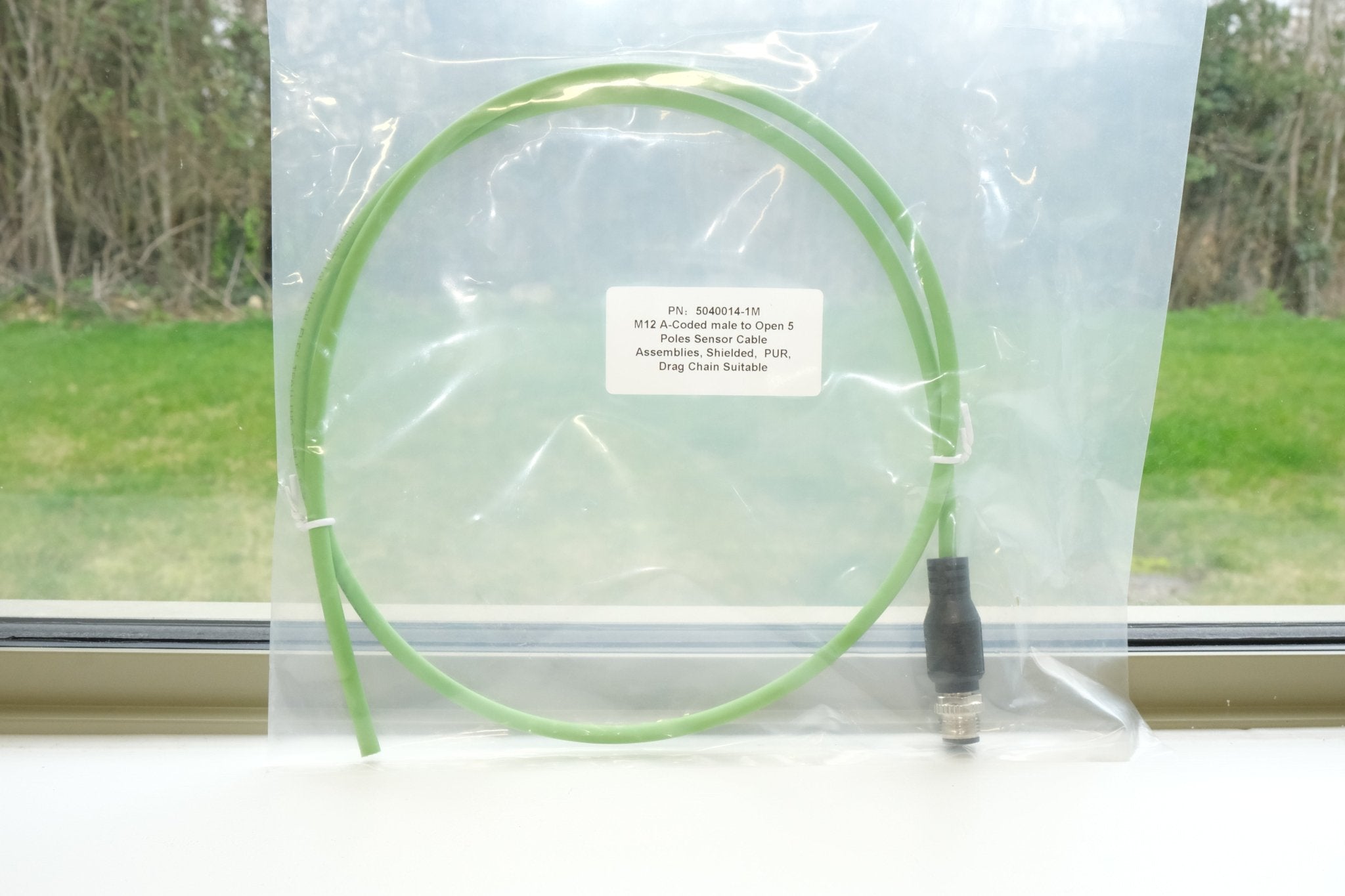 Green cable with a connector on a clear plastic stand against a window background