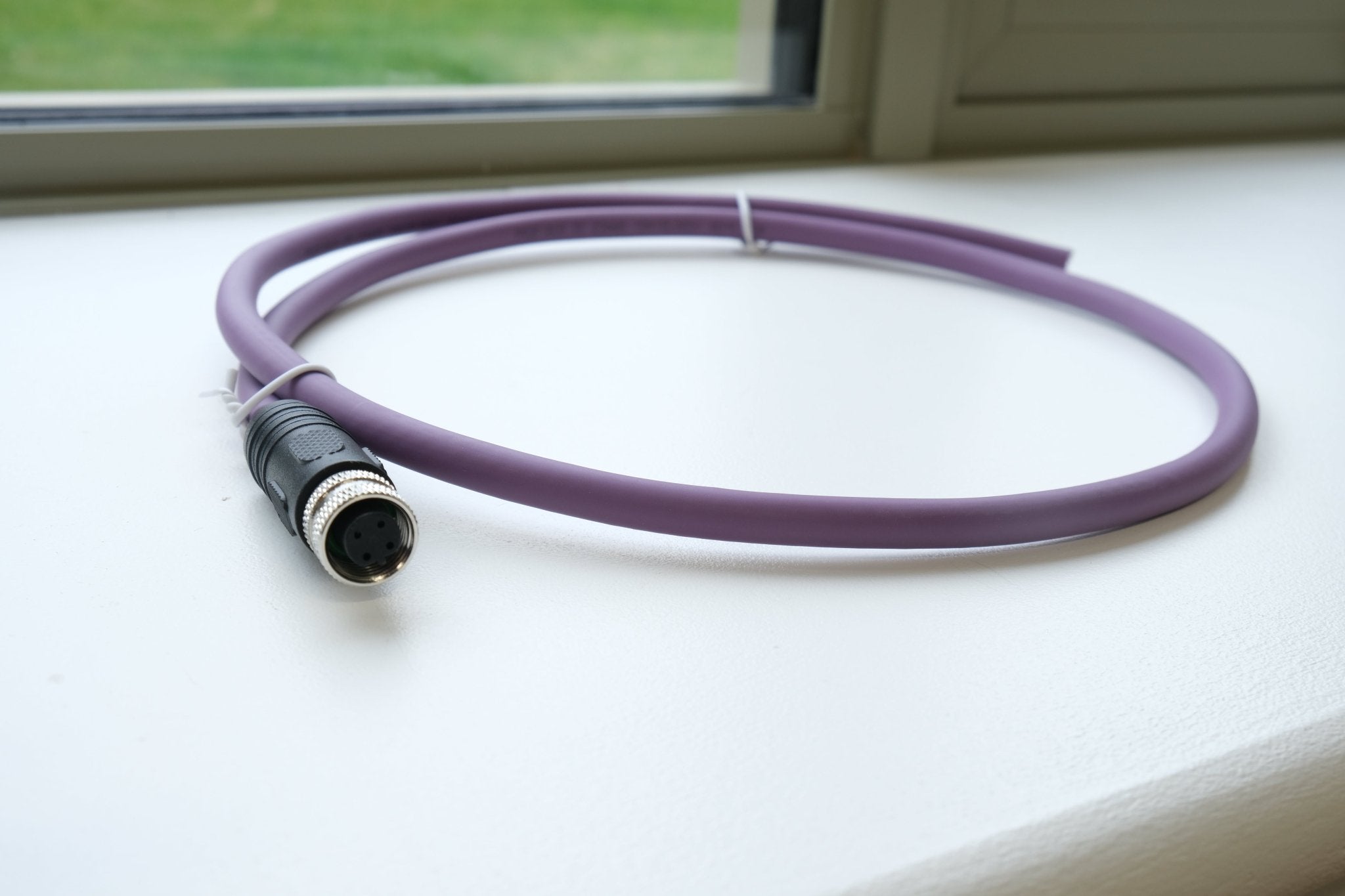 Purple cable with a black connector on a white surface near a window