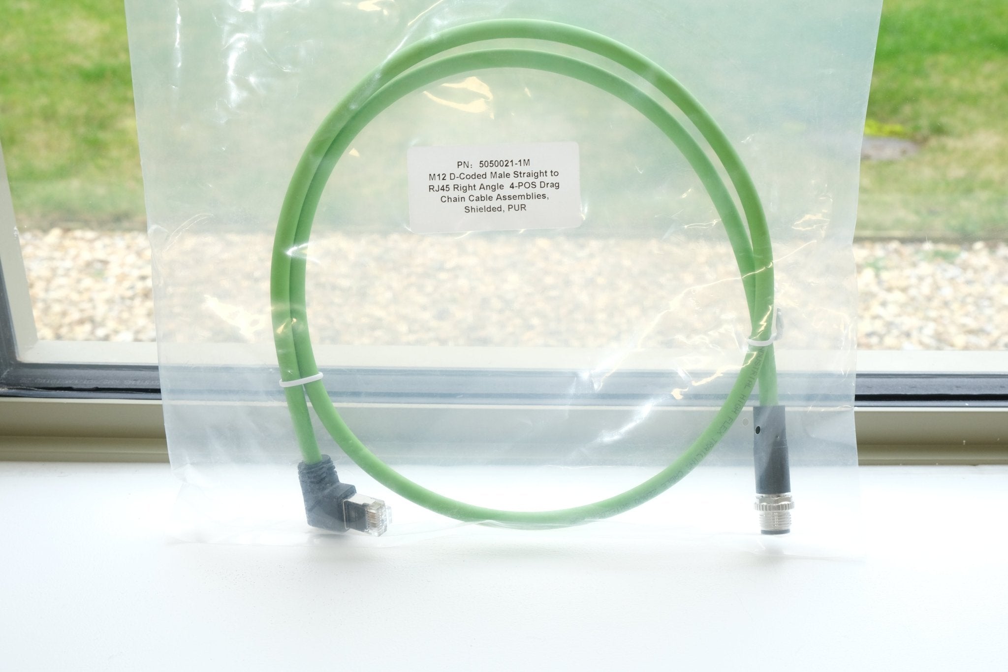 Green cable coiled inside a clear plastic bag with a label on a white surface.
