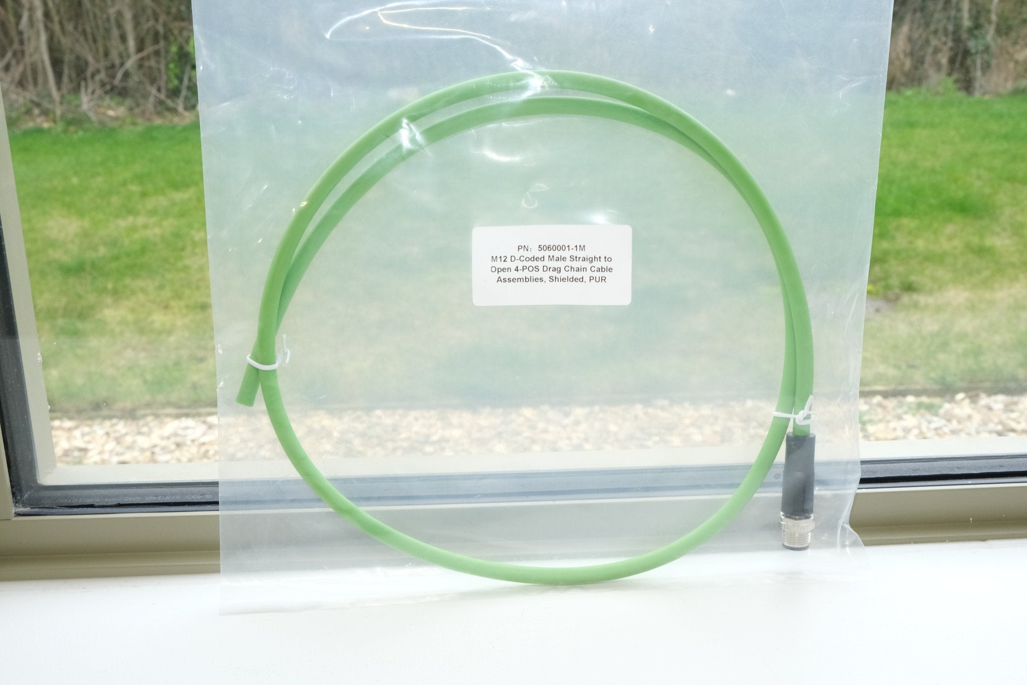 Green cable coiled on a white surface with a window in the background