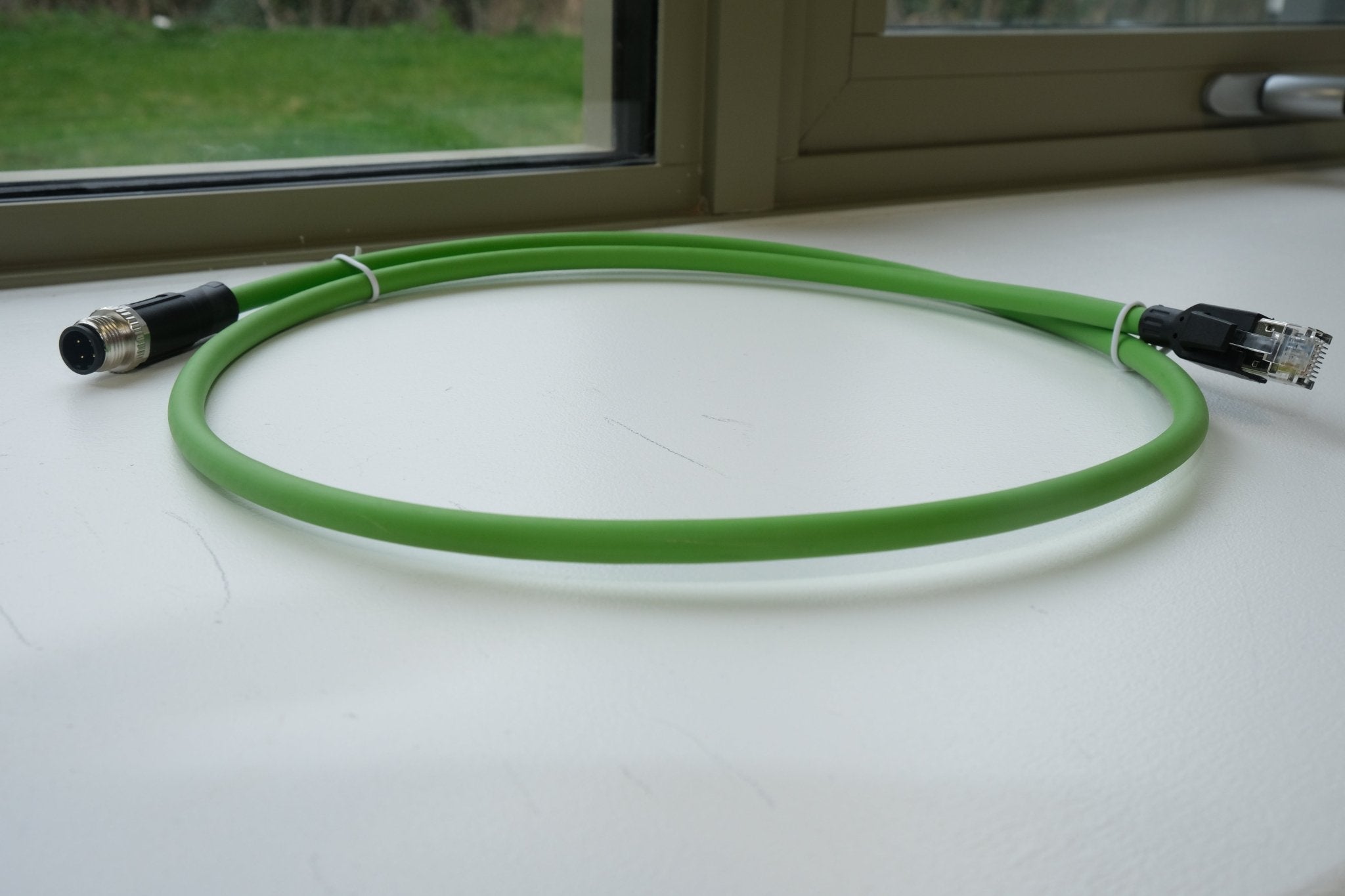Green cable with connectors on a white surface near a window