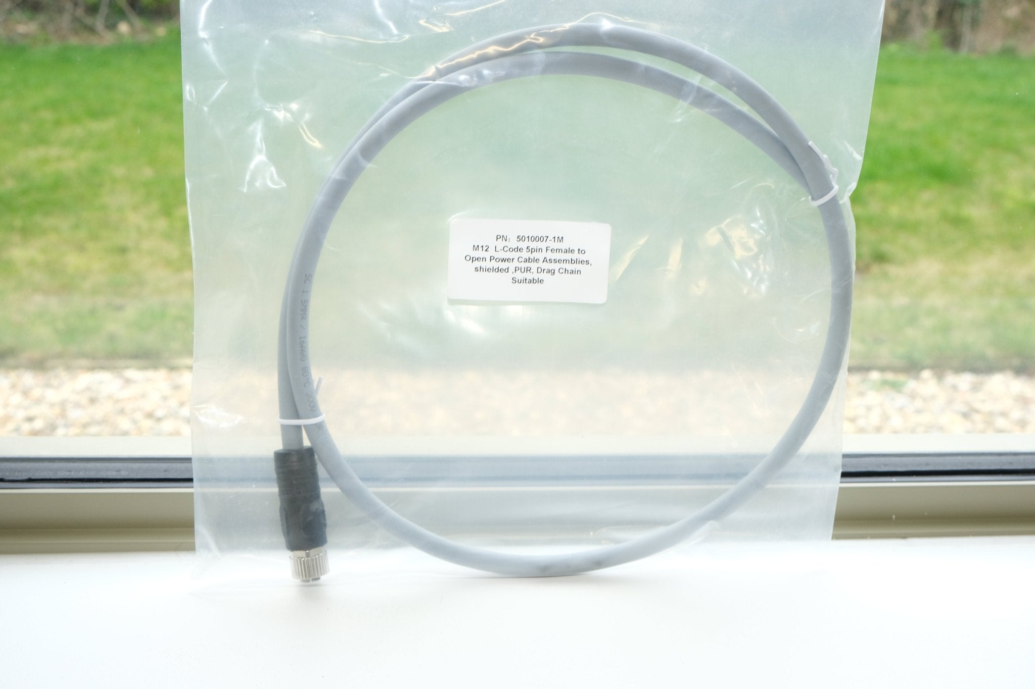 Clear cable with a label on a white surface, with a window and grass outside.