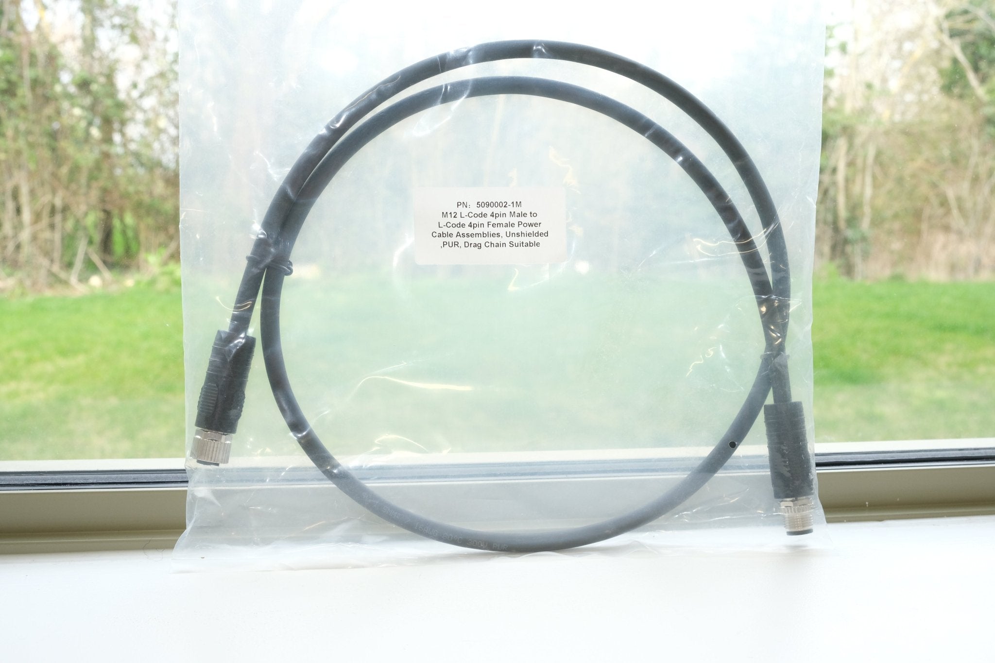 Black circular object in a clear plastic bag on a windowsill with greenery outside.