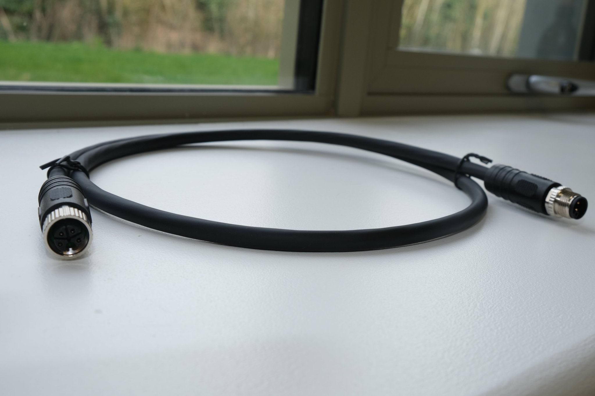 Black cable with connectors on a light surface, possibly inside a vehicle.
