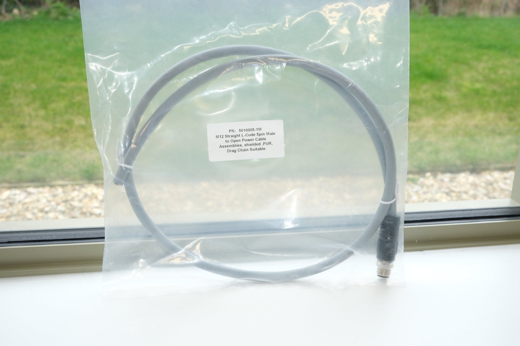 Cable in clear packaging on a windowsill with grass outside