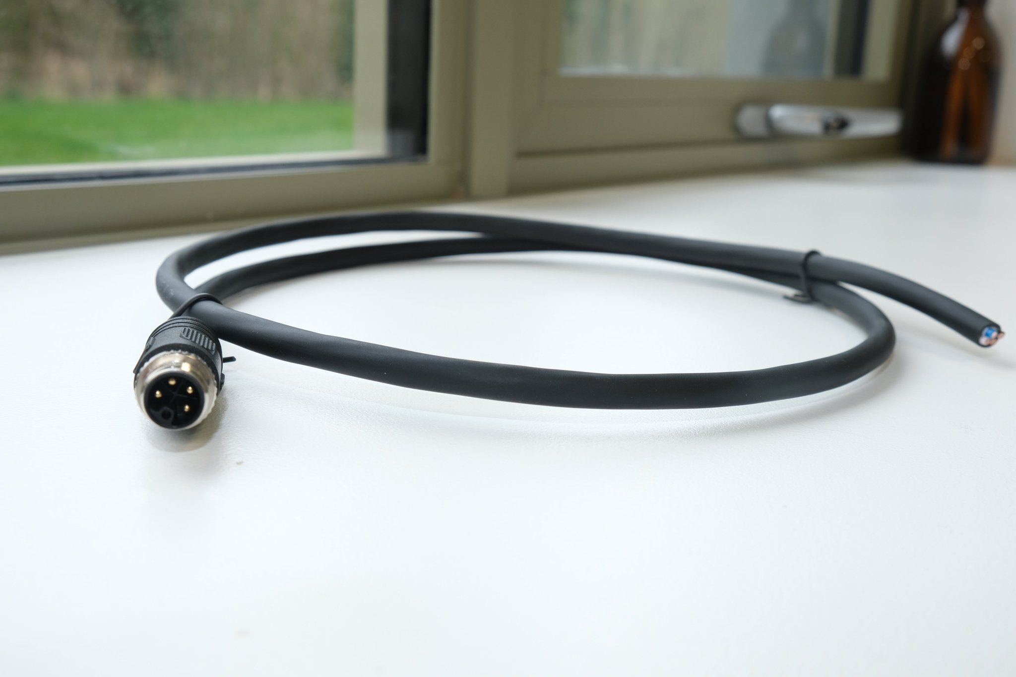 Black cable with a connector on a white surface near a window