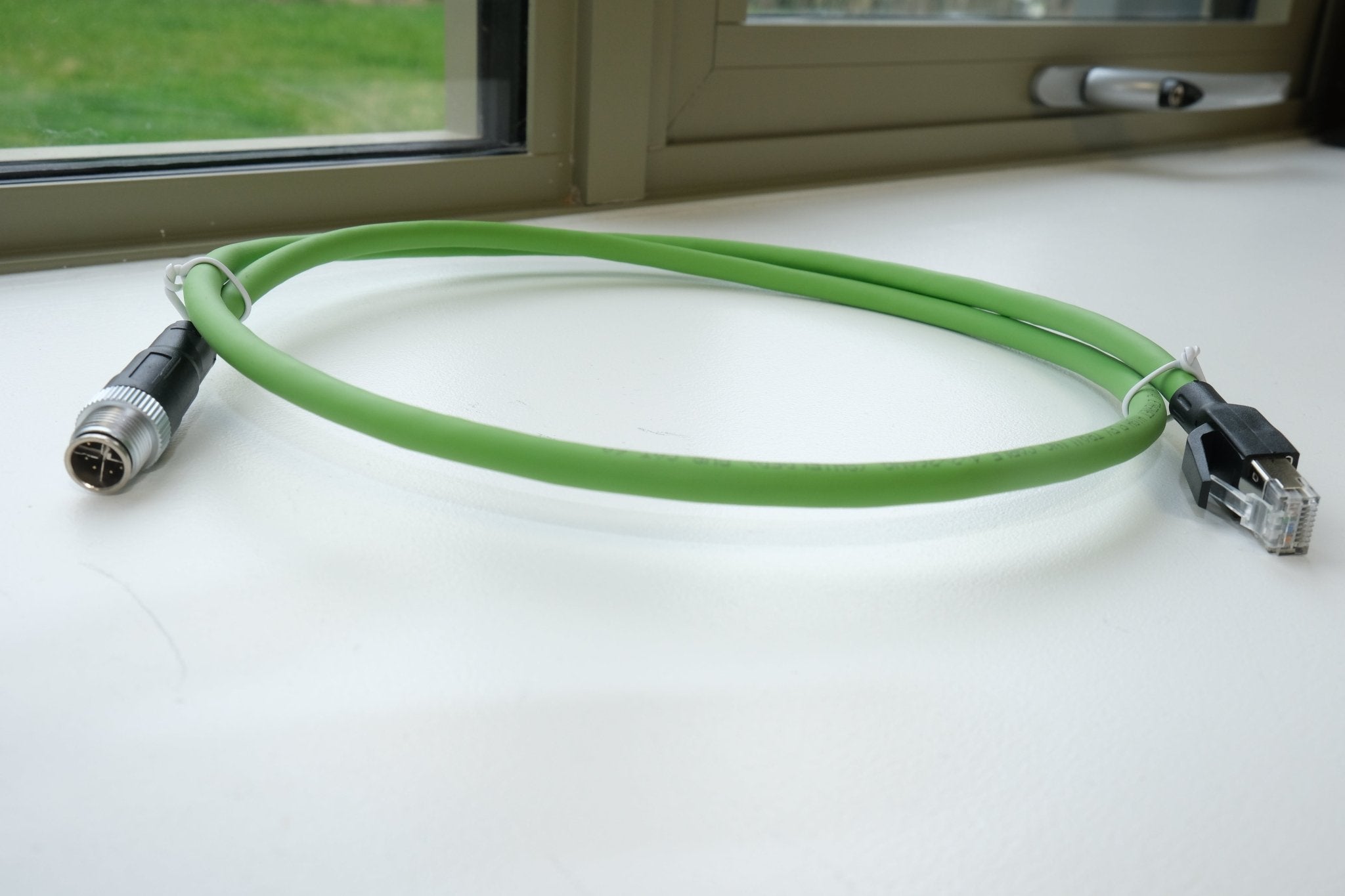 Green cable with connectors on a white surface near a window