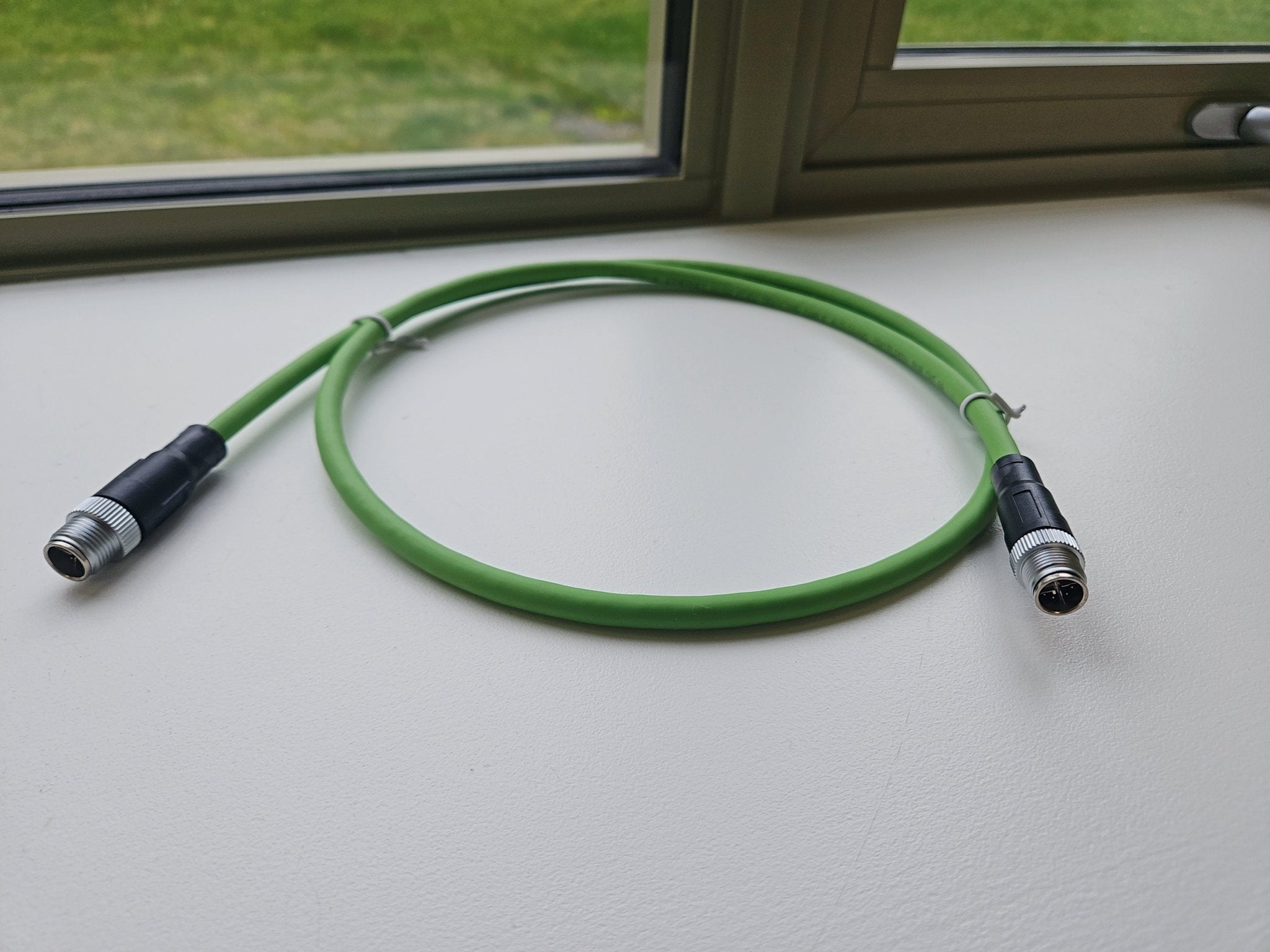 Green cable with connectors on a light surface, window in the background