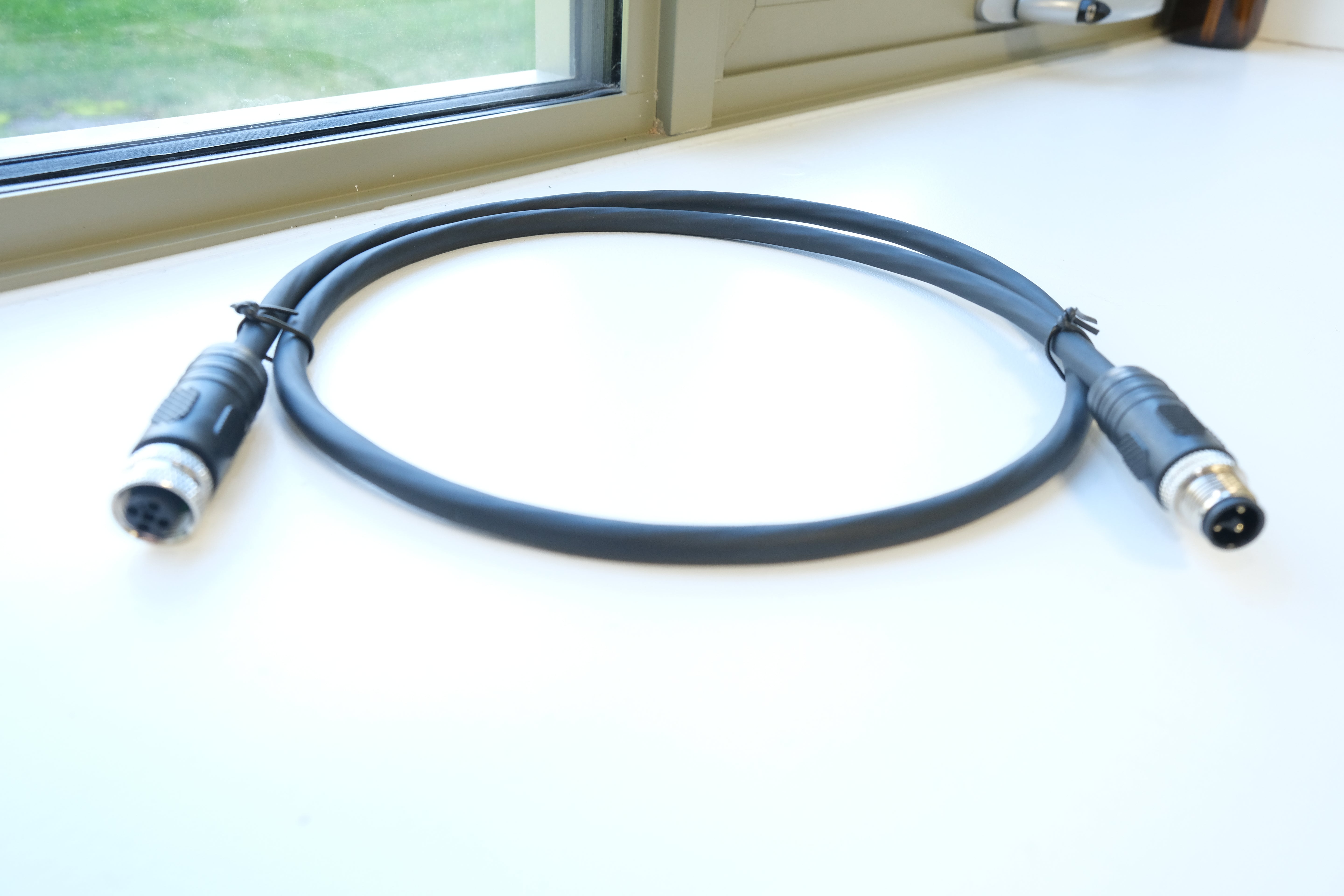 Black cable with connectors on a white surface near a window