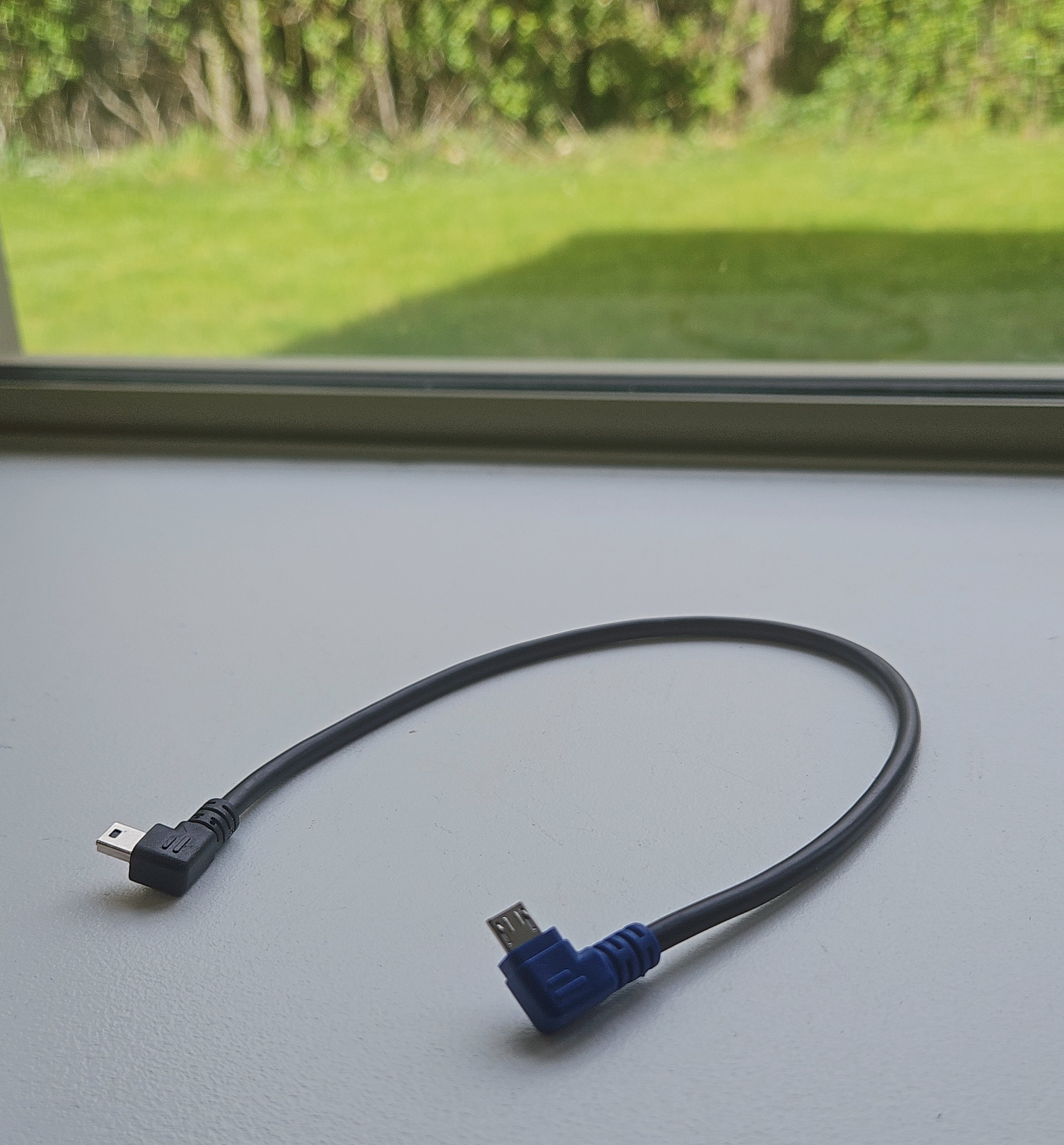USB cable with angled connector on a flat surface with a window in the background