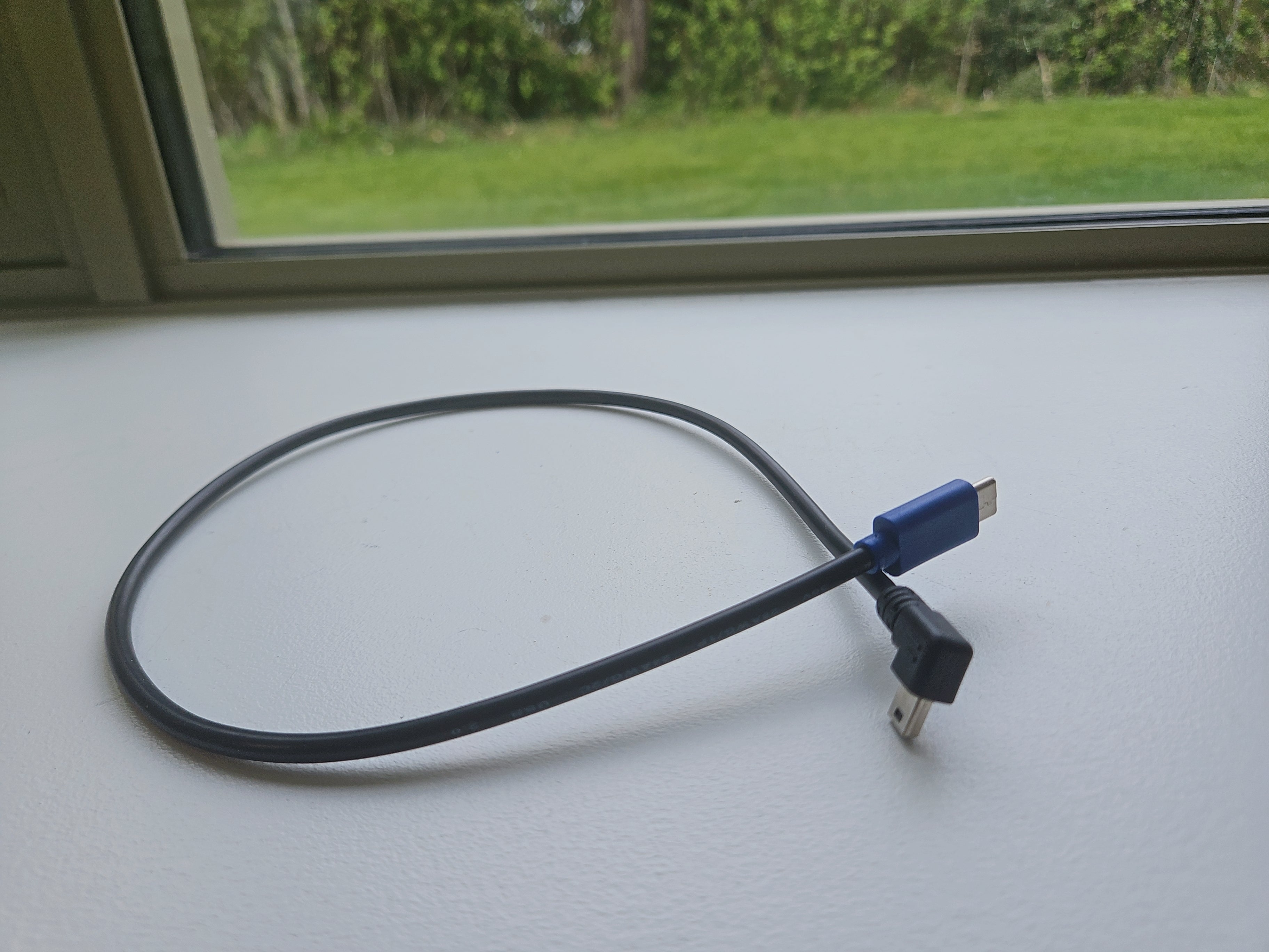 Black USB cable with blue connector on a white surface near a window