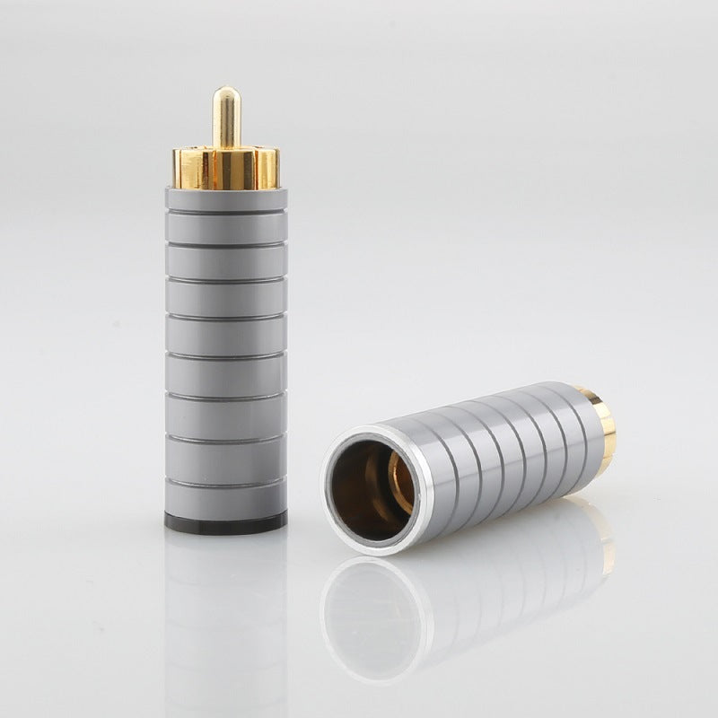 Two cylindrical metal connectors with gold and bronze ends on a reflective surface.