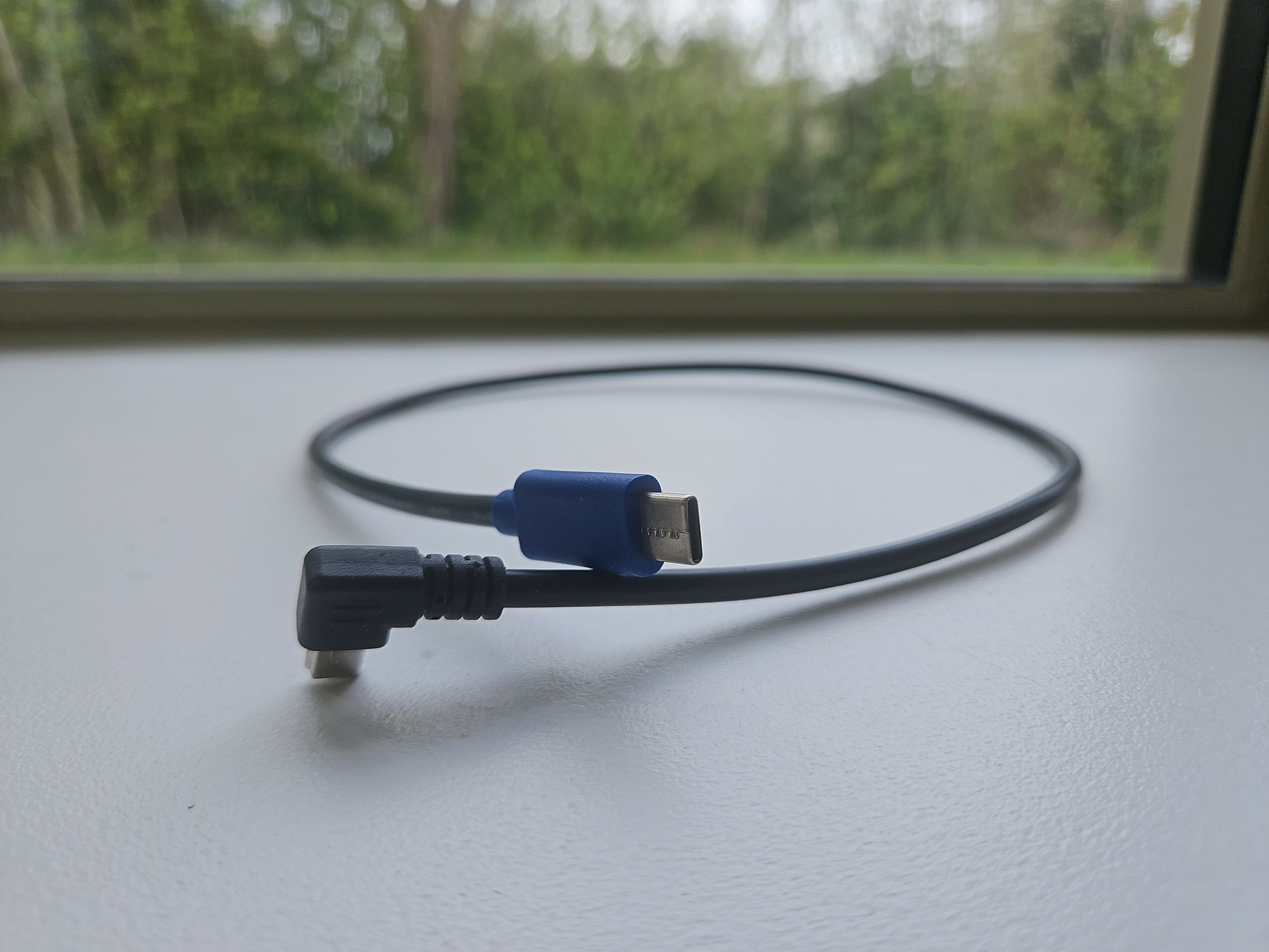 Black USB cable with blue connector on a light surface with a blurred green outdoor background