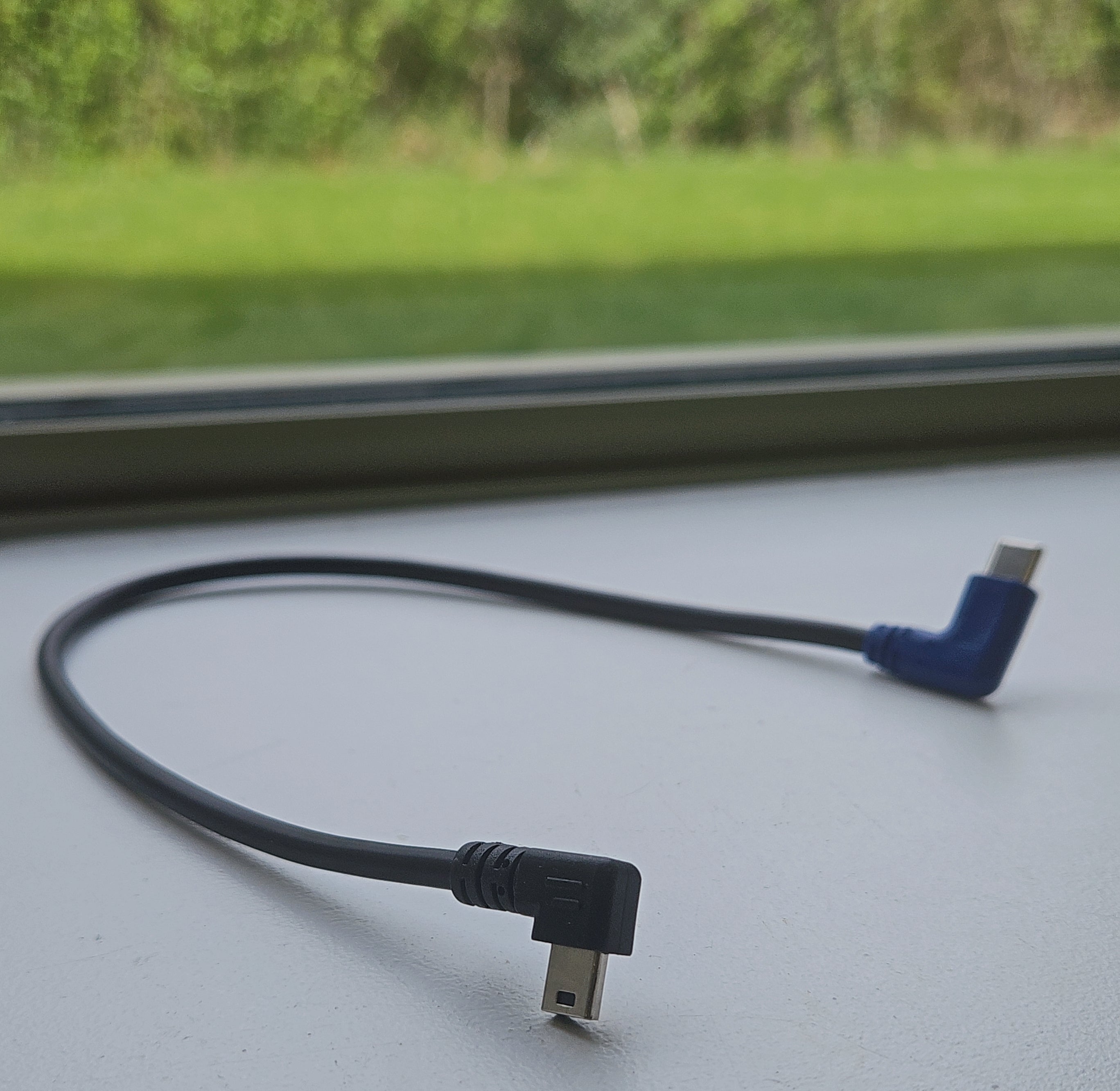 USB cable with black and blue connectors on a light gray surface with a blurred green outdoor background.