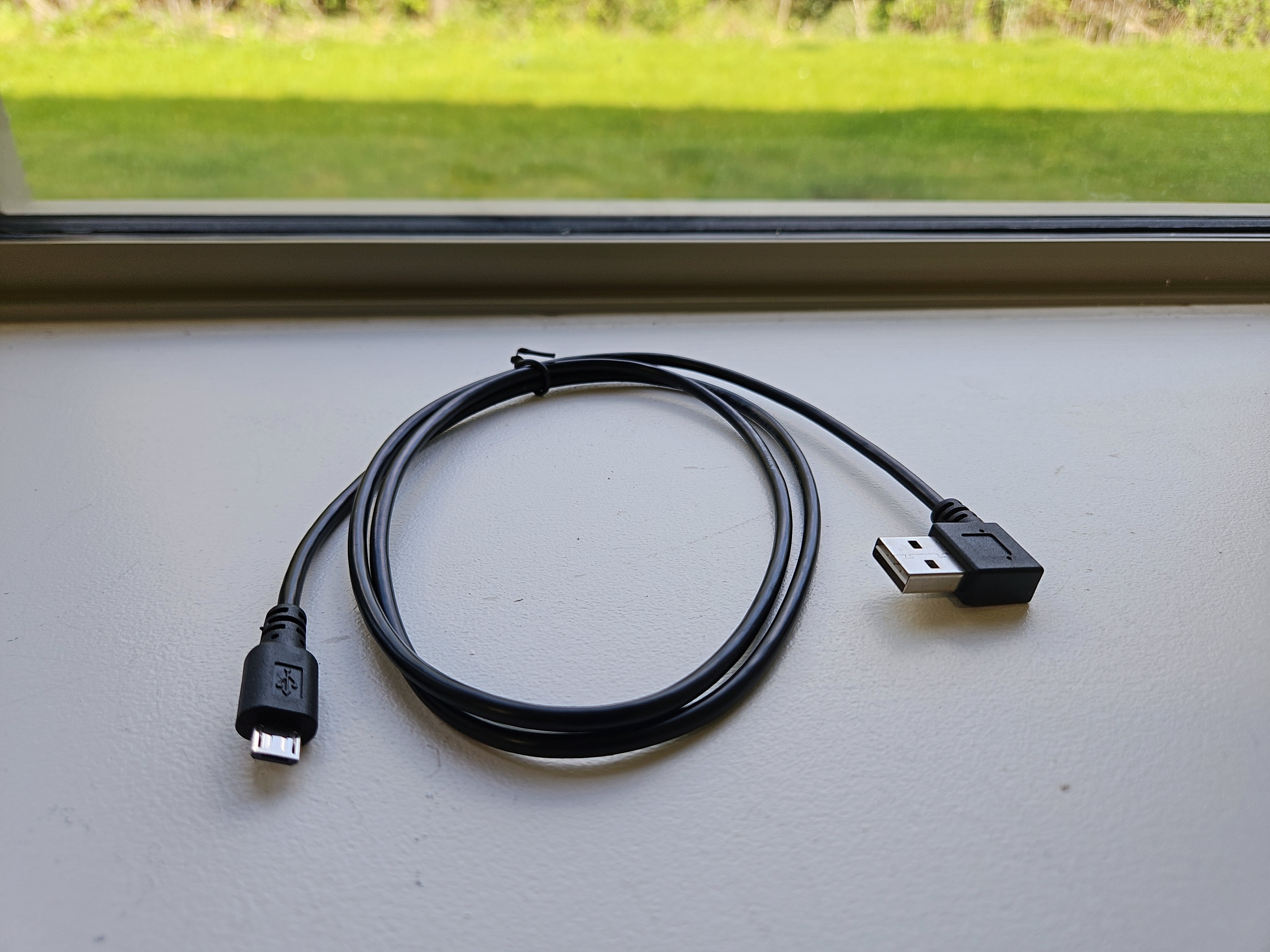 Black USB cable with connectors on a light gray surface with a window in the background.